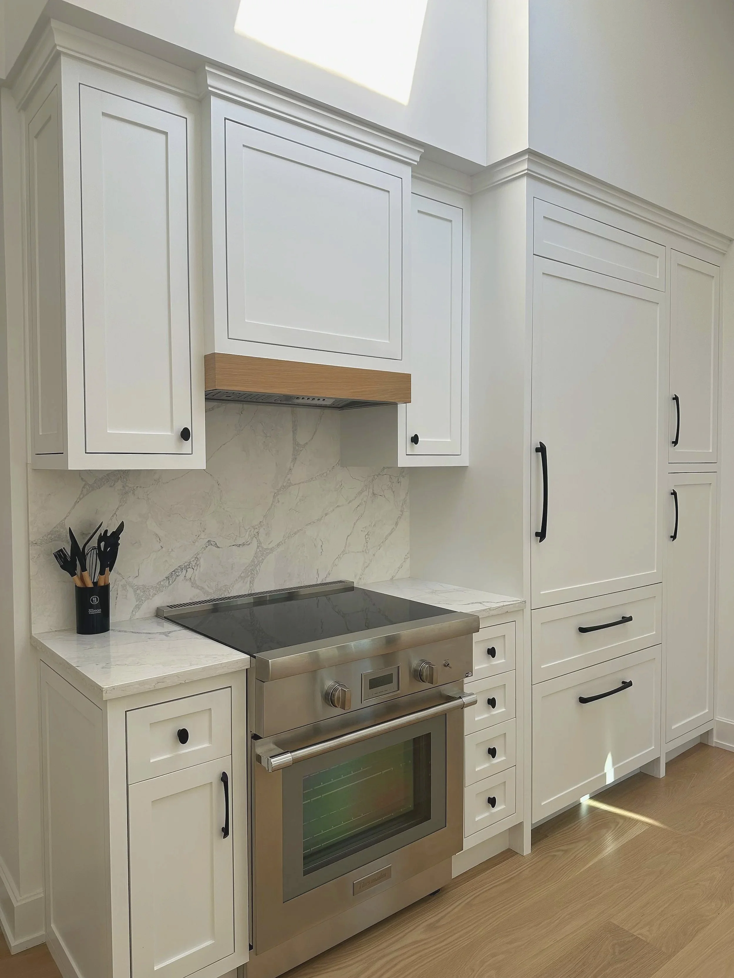 White kitchen with cabinets, marble countertop, stainless steel oven, black handles, and a utensil holder.