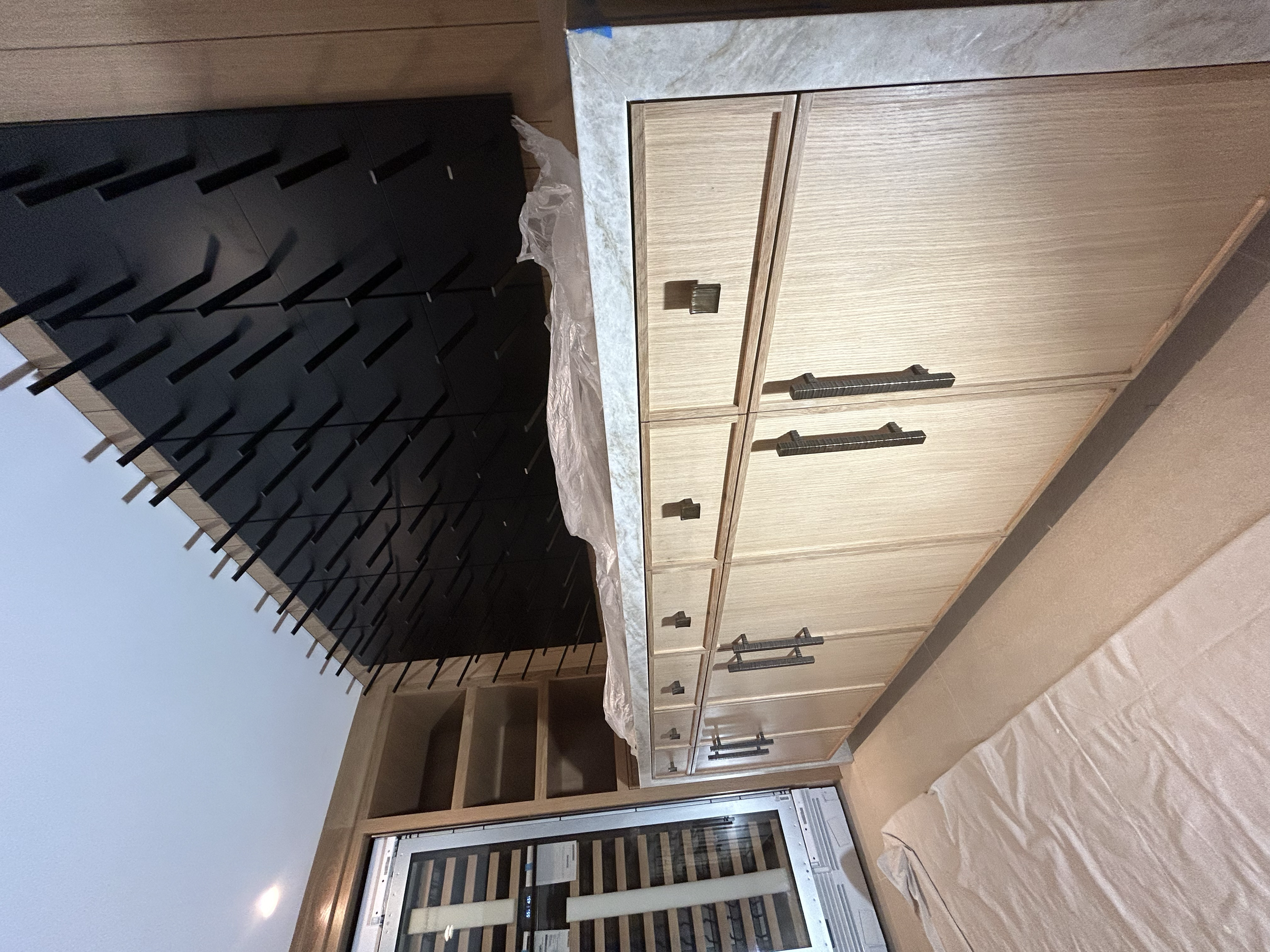 Kitchen cabinets, one in natural wood finish, and another in black with modern handles, with some construction or remodeling supplies nearby.