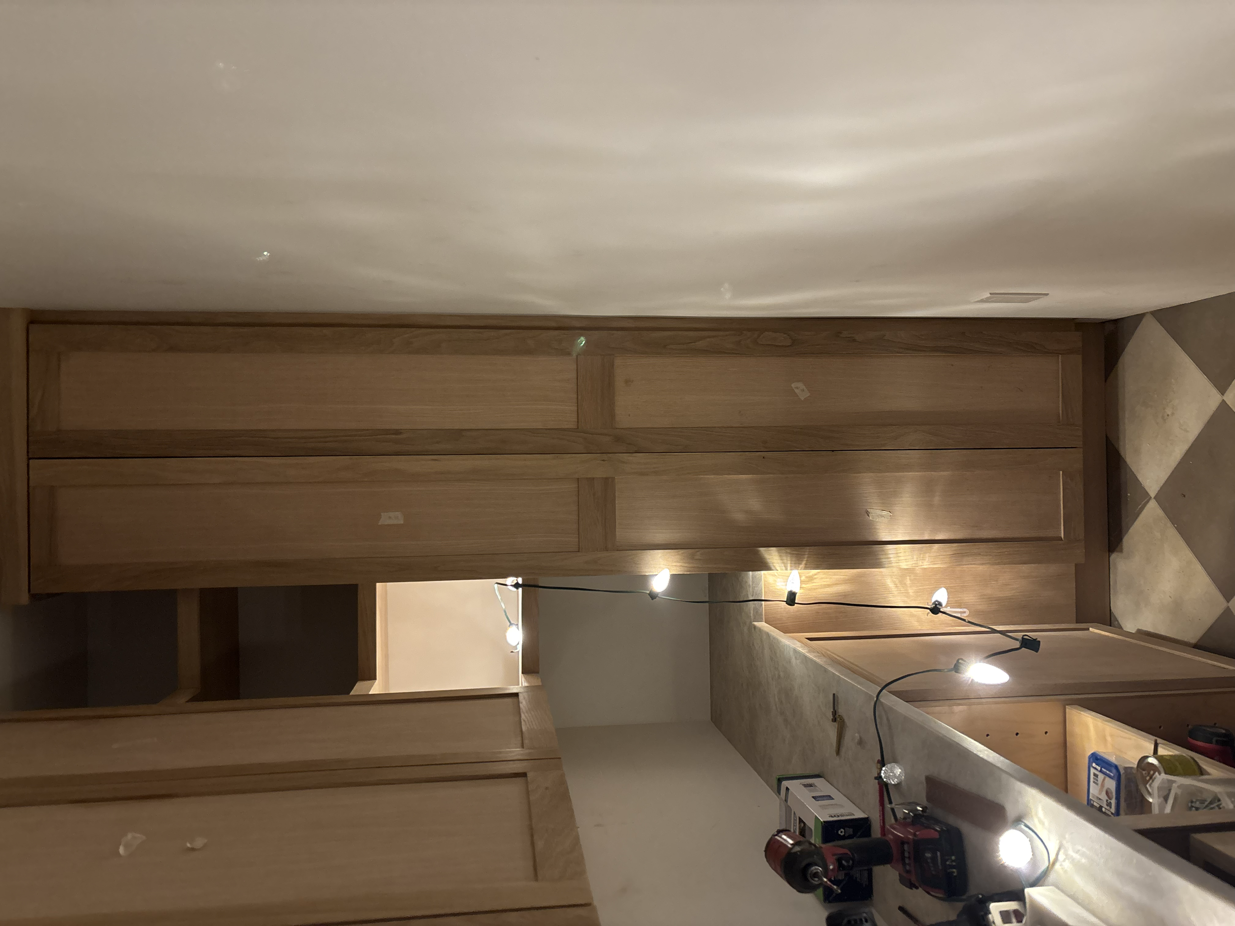 Wooden cabinets are being installed in a kitchen with construction tools and work lights.