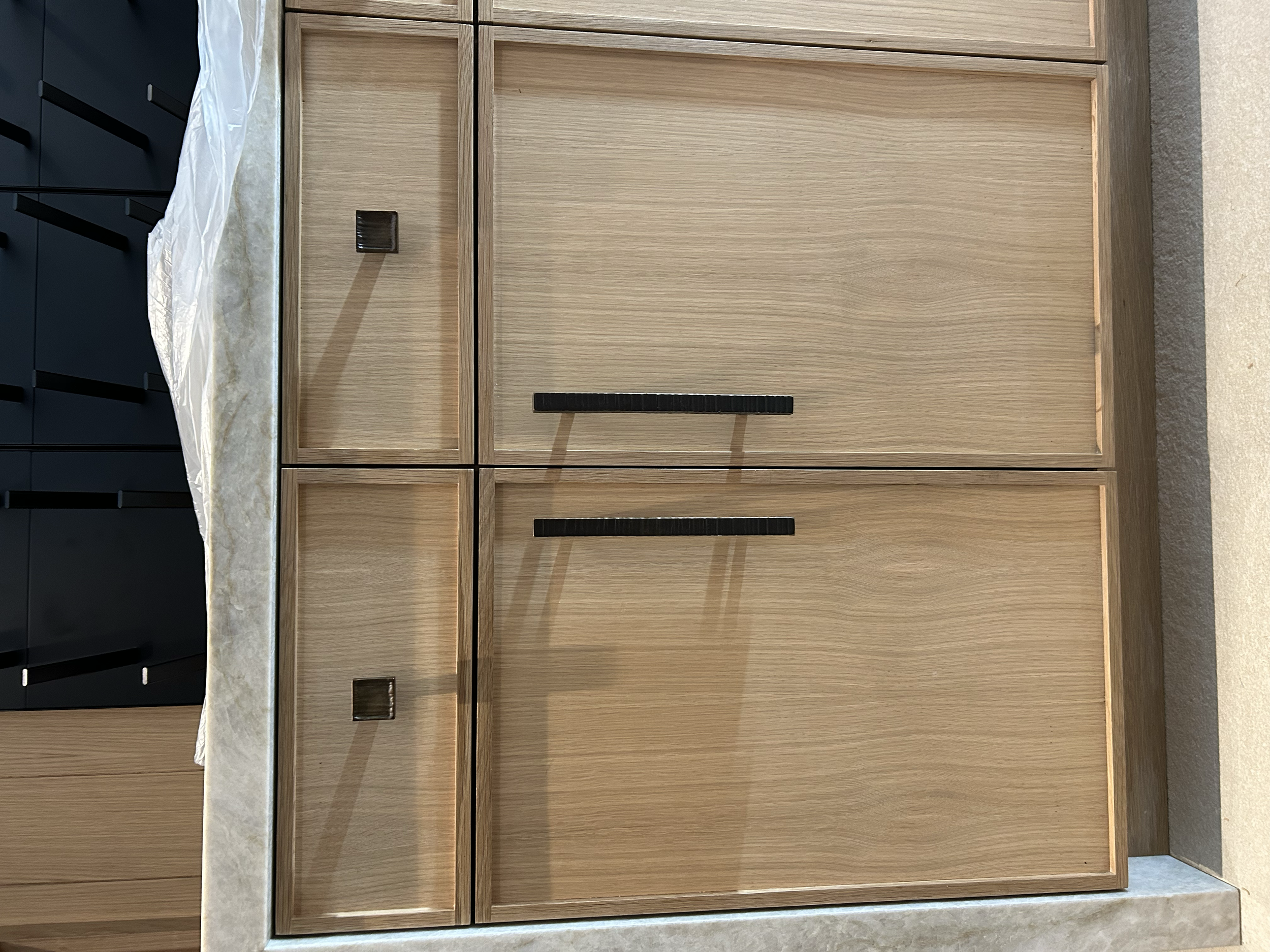 A wooden sideboard with black handles, placed against a wall with a countertop on top.