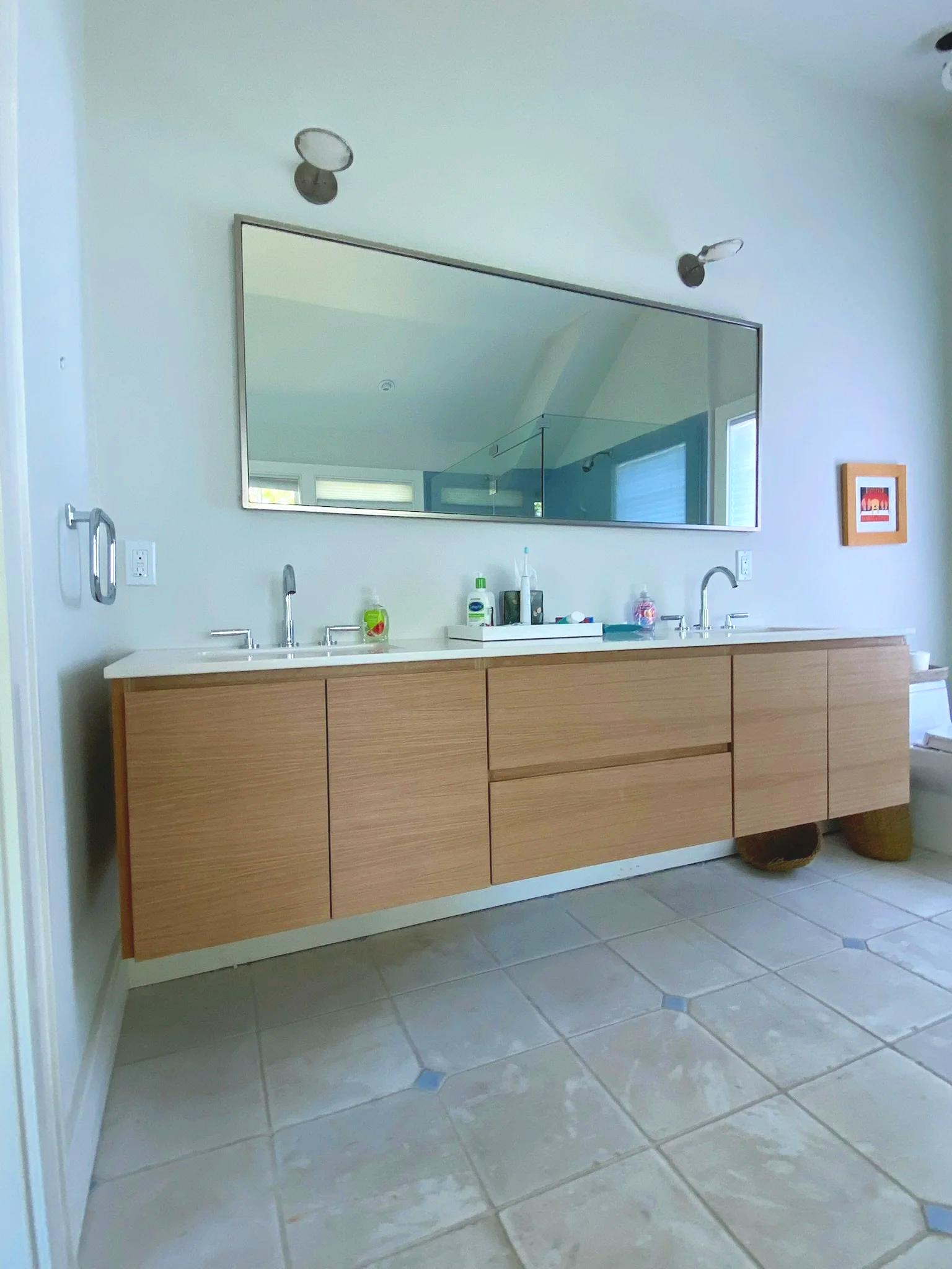 Bathroom with a double vanity, large mirror, wall lights, and beige tiled floor. Custom cabinet.