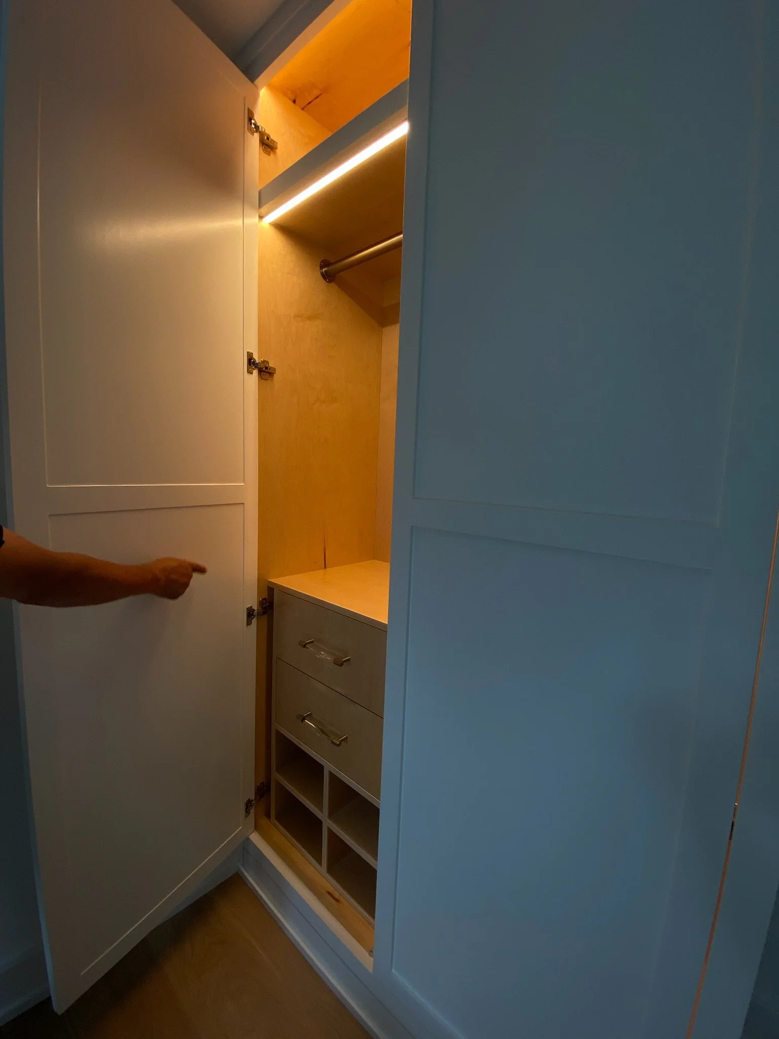 Open white kitchen cabinet with wooden interior, drawers, cubbies, and hanging rod.