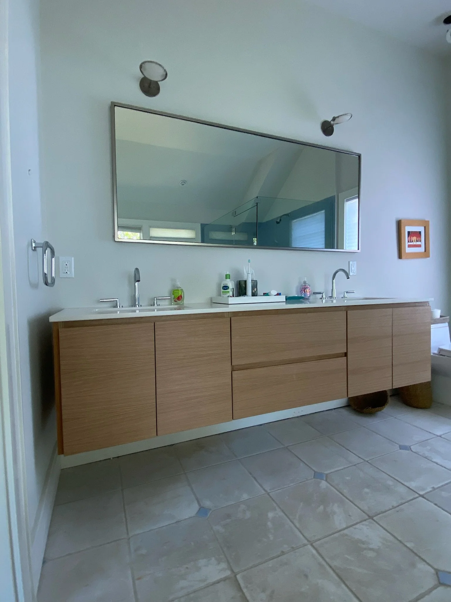 A modern bathroom with a double sink vanity, large wall mirror, and beige tiled floor.