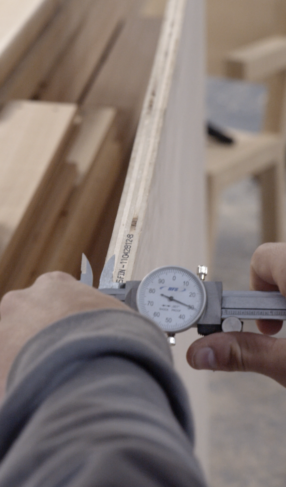 Close-up of a person measuring the thickness of a piece of wood with a dial caliper.