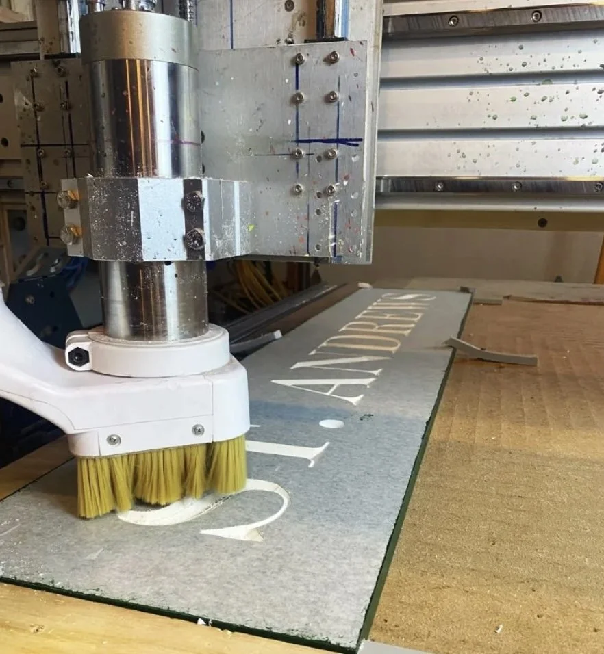 A machine with a yellow brush cleaning or finishing a sign that says 'L' and 'ART'. CNC Machine. Signs.