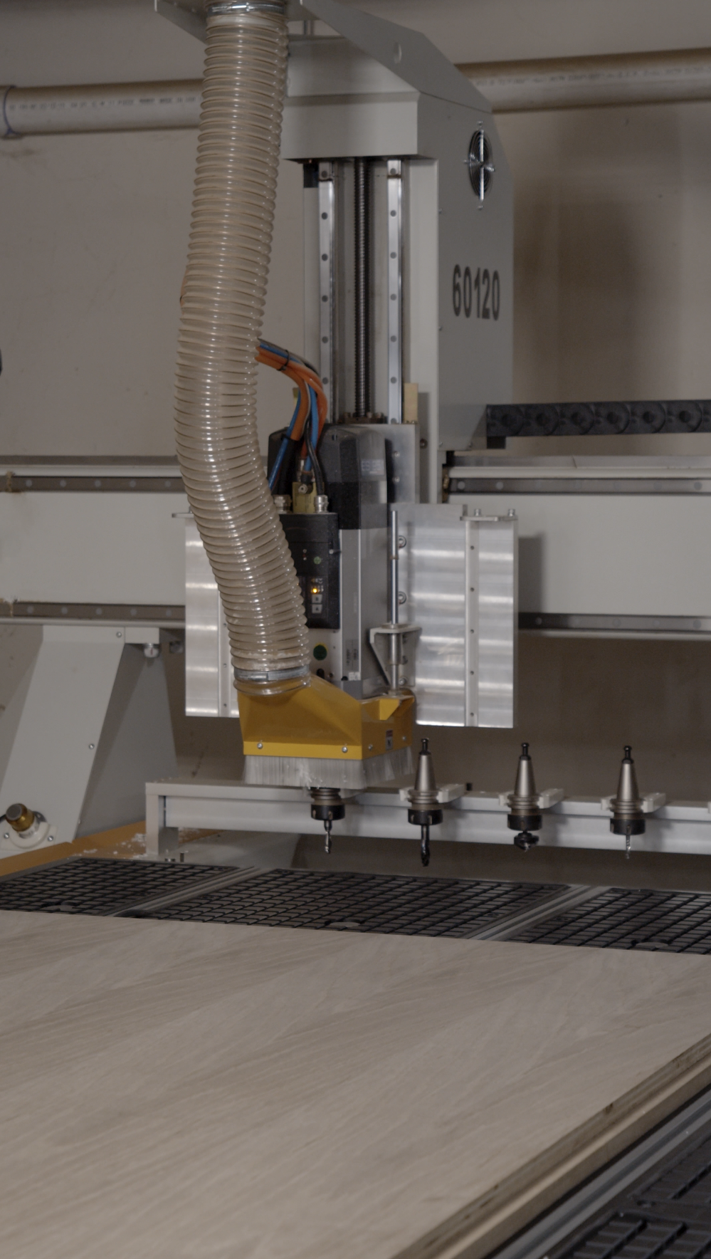 A CNC woodworking machine with a vacuum hose, four drill bits, and a work surface with wooden panels.