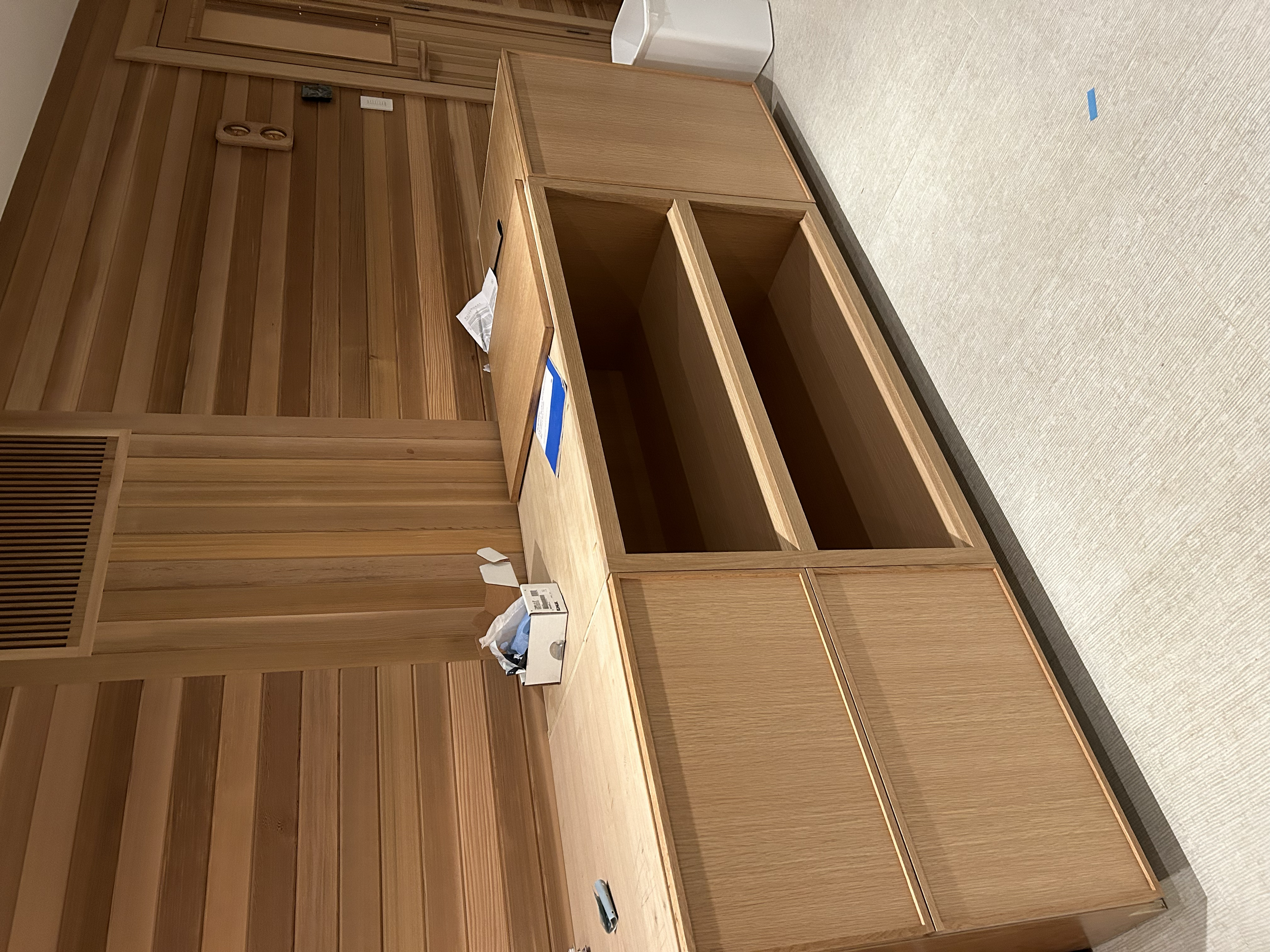 Empty wooden cabinet and desk with some paper and tissue on top, in a room with wood-paneled walls and light-colored carpet.