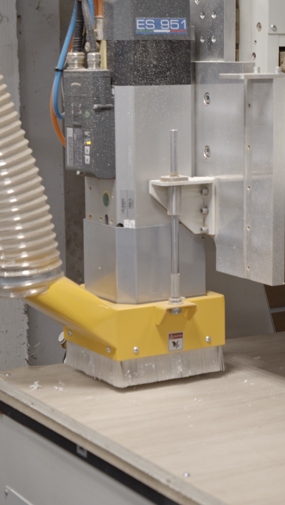 A woodworking machine shaping or sanding a piece of wood, with dust and wood shavings visible around.