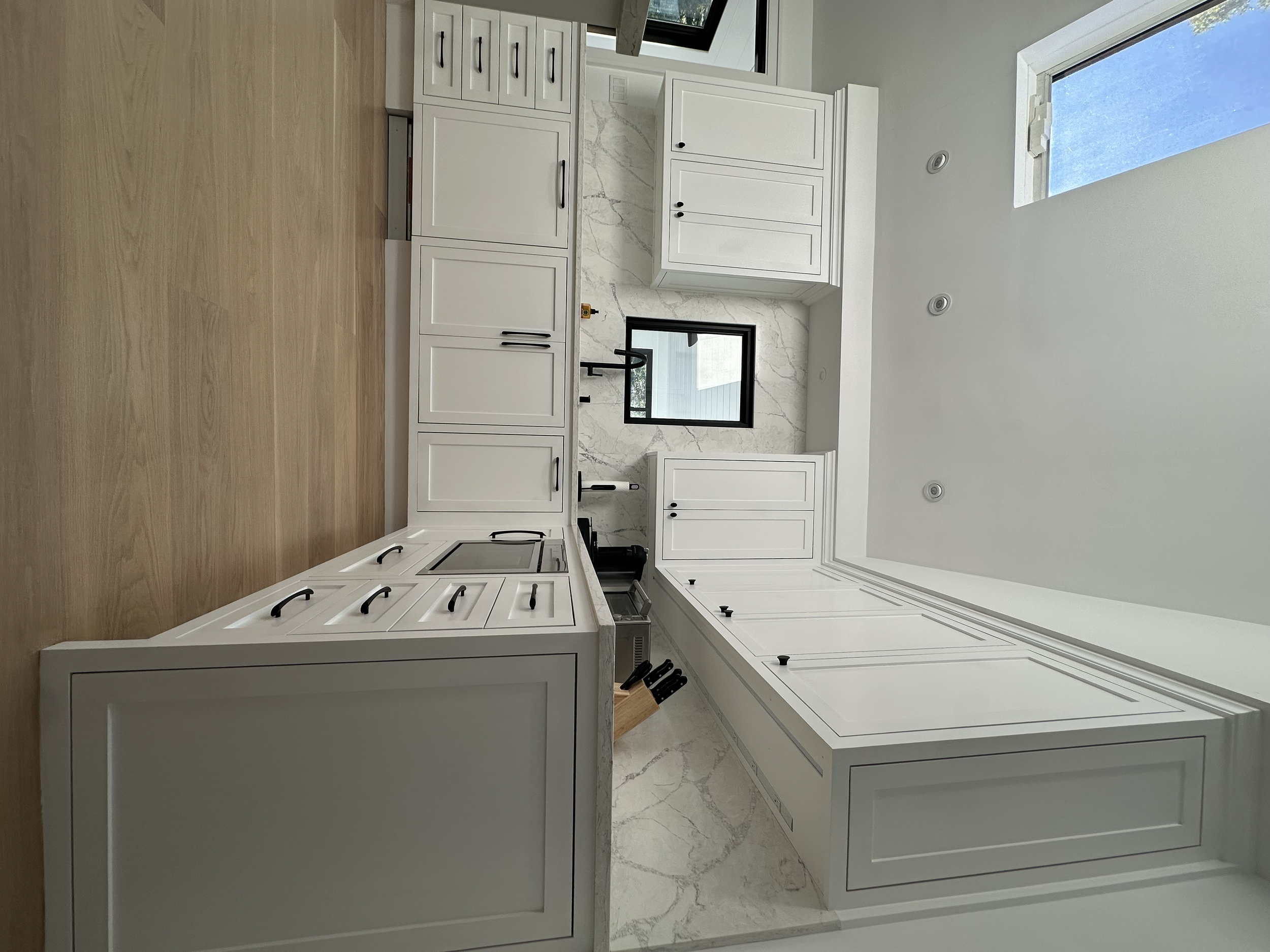 Modern kitchen with white cabinets, marble backsplash, wooden floor, black faucet, and large window.