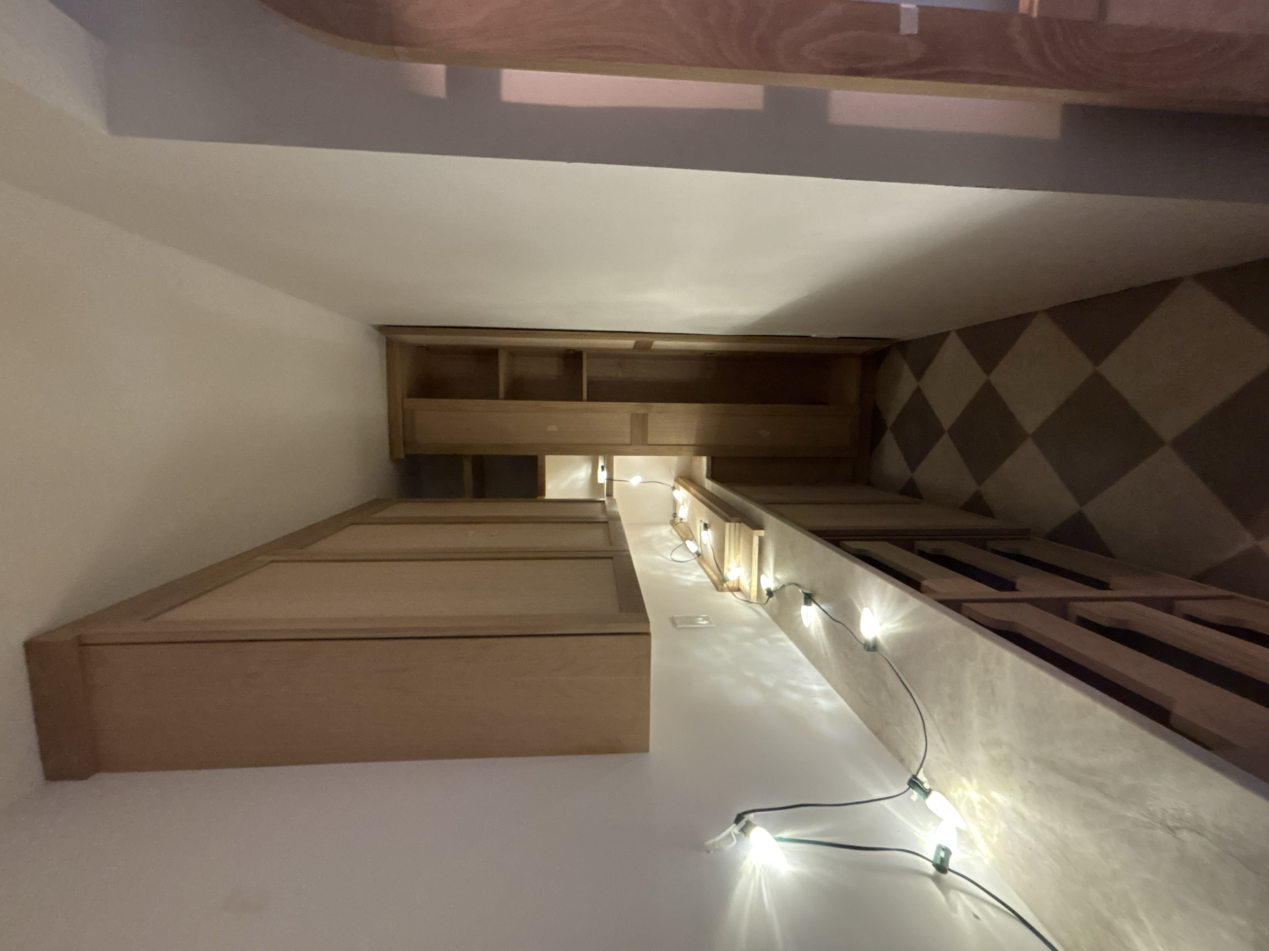 Interior view of a hallway in a home with wooden storage units and a string of white holiday lights along the countertop.