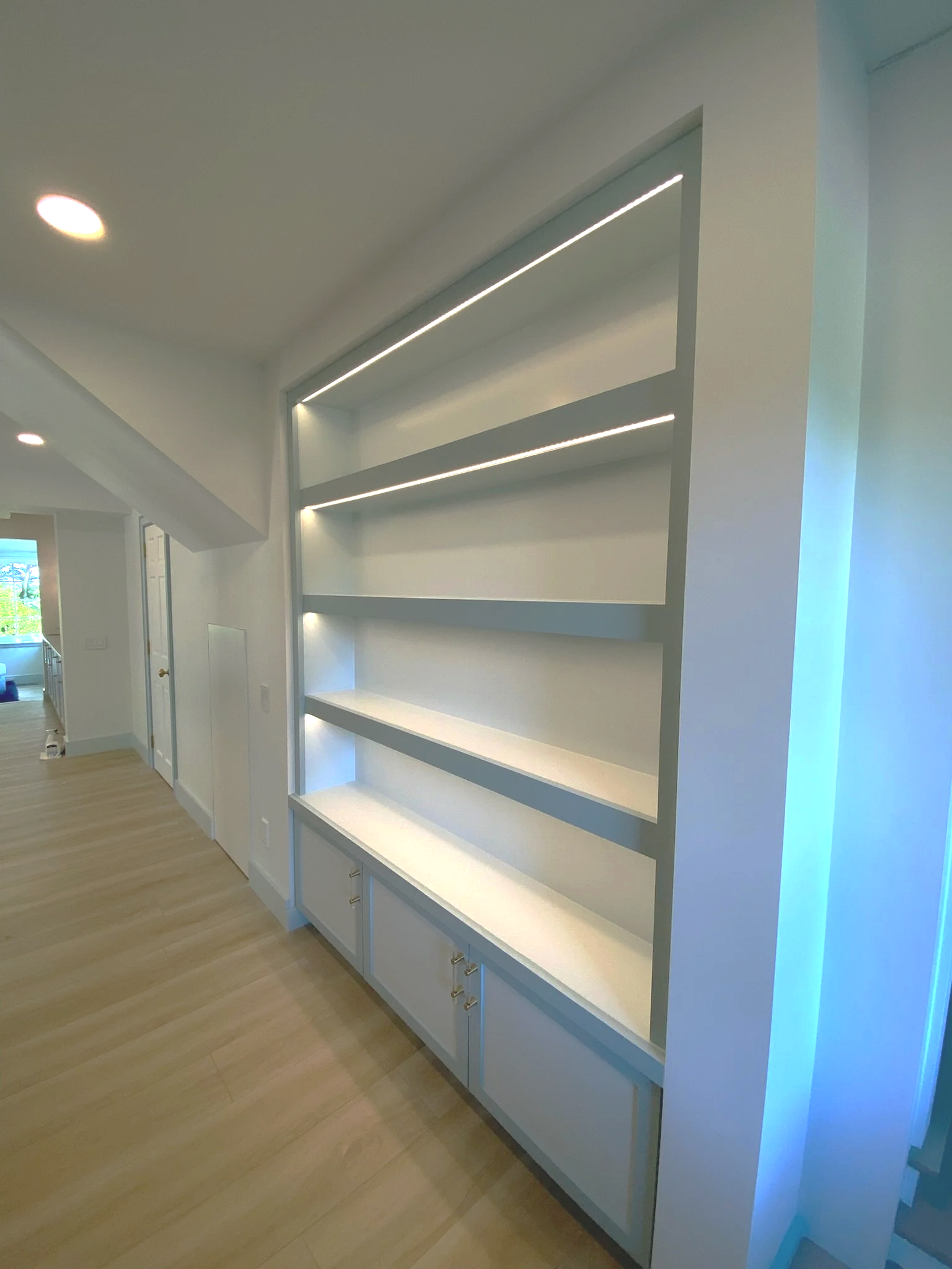 Empty white built-in bookshelf with LED strip lighting in a modern home interior. Custom cabinet.
