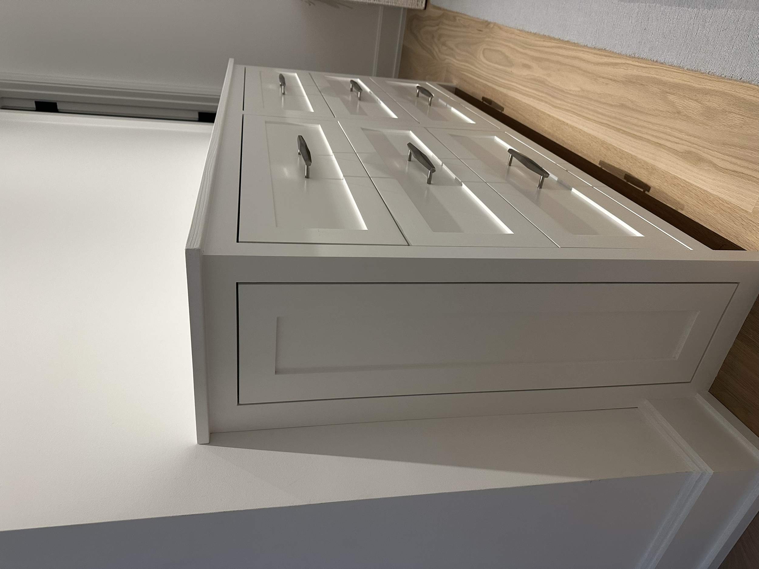 A white vintage-style dresser with multiple drawers and silver handles, placed against a light-colored wall on a wood floor. Custom cabinet.