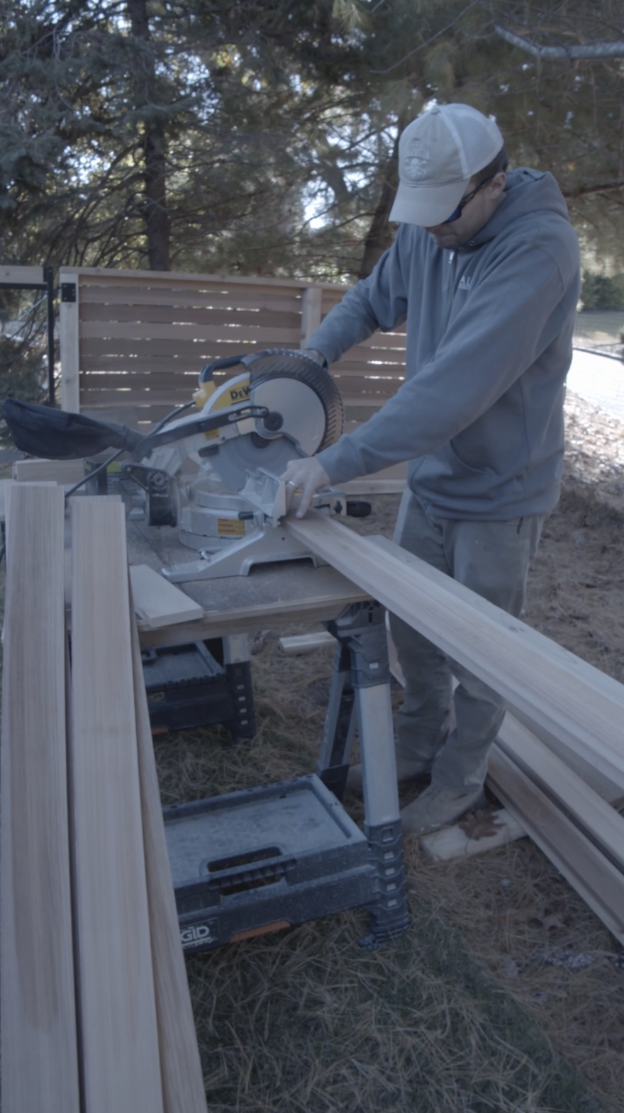 Man using a miter saw to cut wood outdoors in a backyard. Fence.