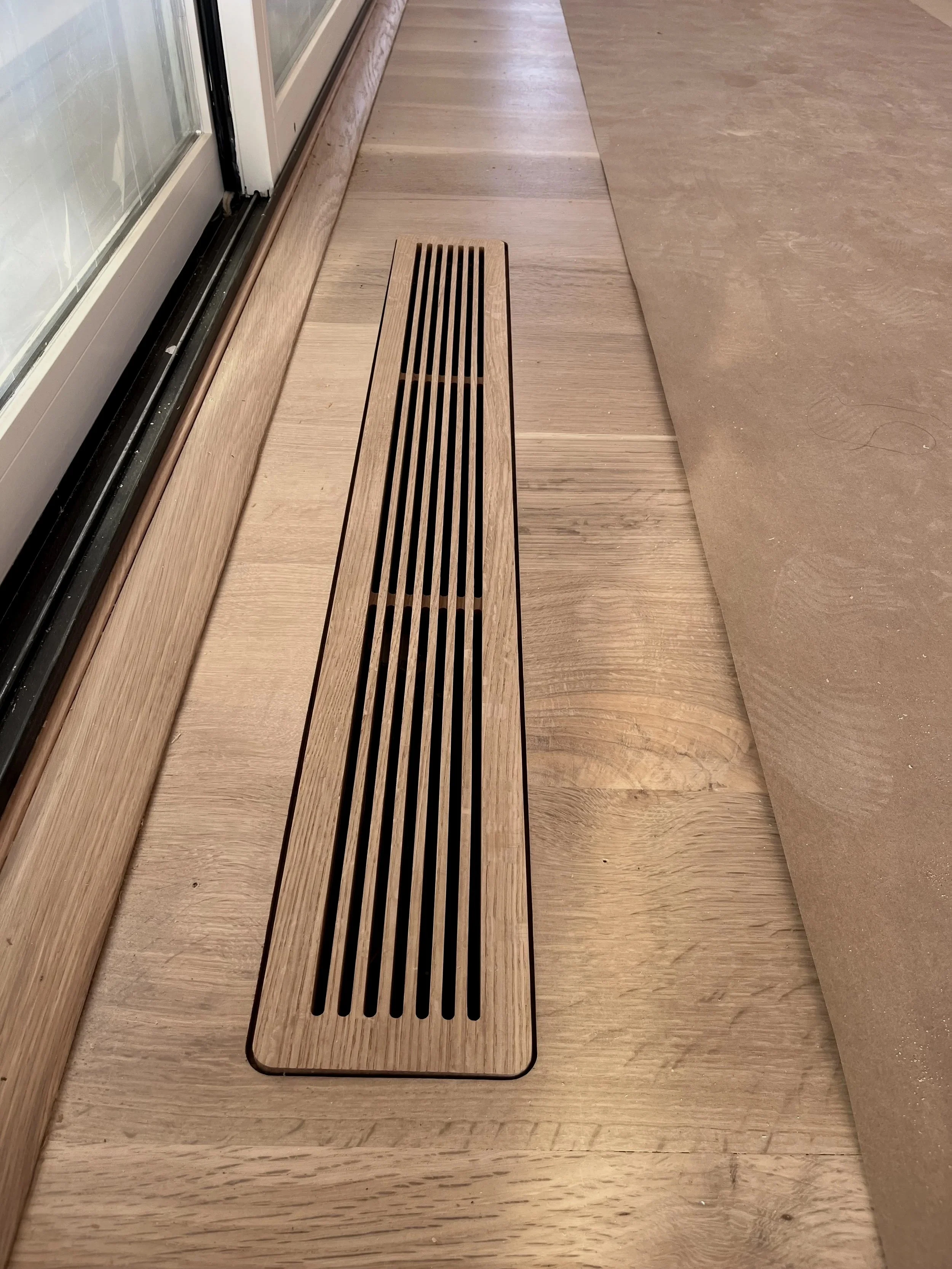 Wooden floor with a metal vent near a glass door, adjacent to a section of flooring covered with brown paper.