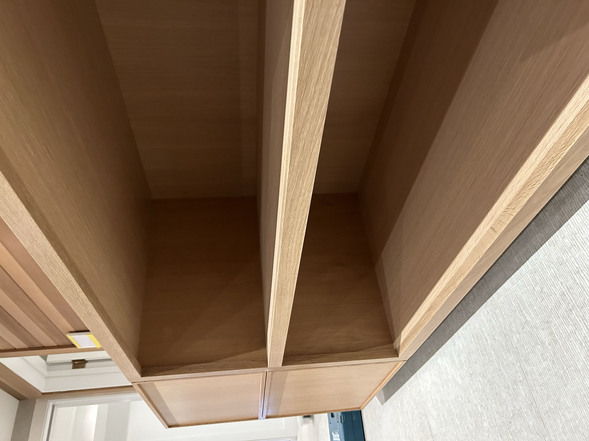 Empty wooden bookshelf with two sections, located in a room with beige carpet and a door in the background.