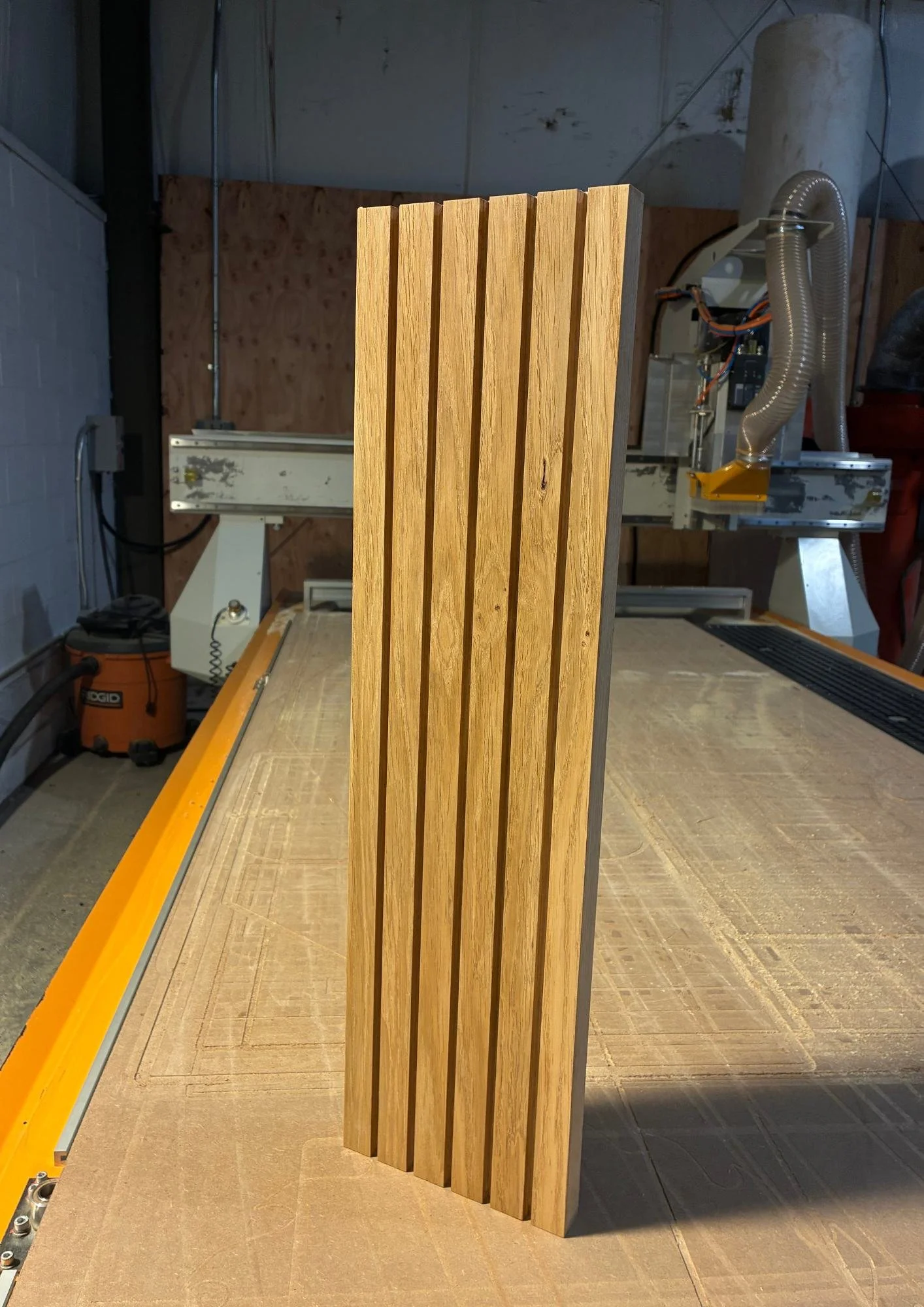 A wooden slatted panel standing upright on a woodworking table in a workshop.