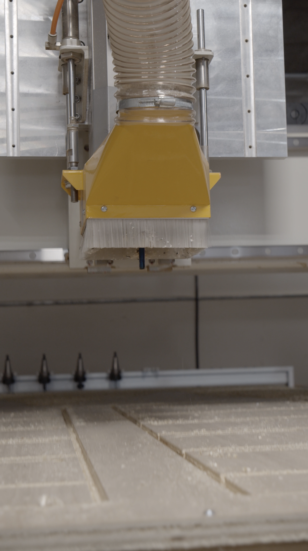 Close-up of an industrial CNC machine with a yellow dust extraction hood and a flexible hose above a metal surface.