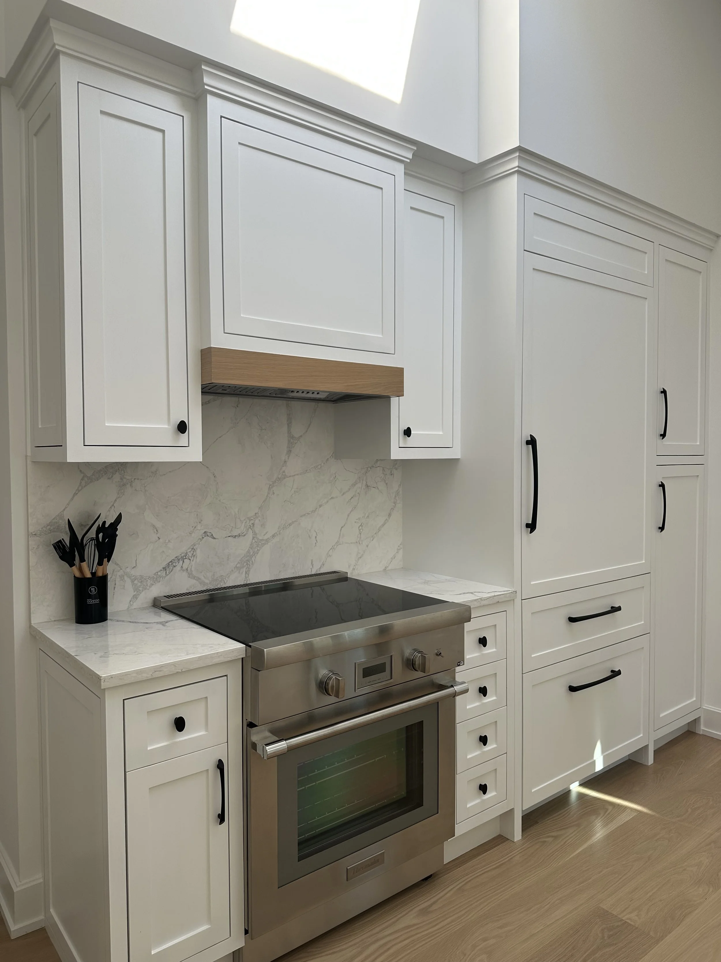 Kitchen with white cabinets, marble countertop and backsplash, stainless steel oven, and black drawer and cabinet handles.