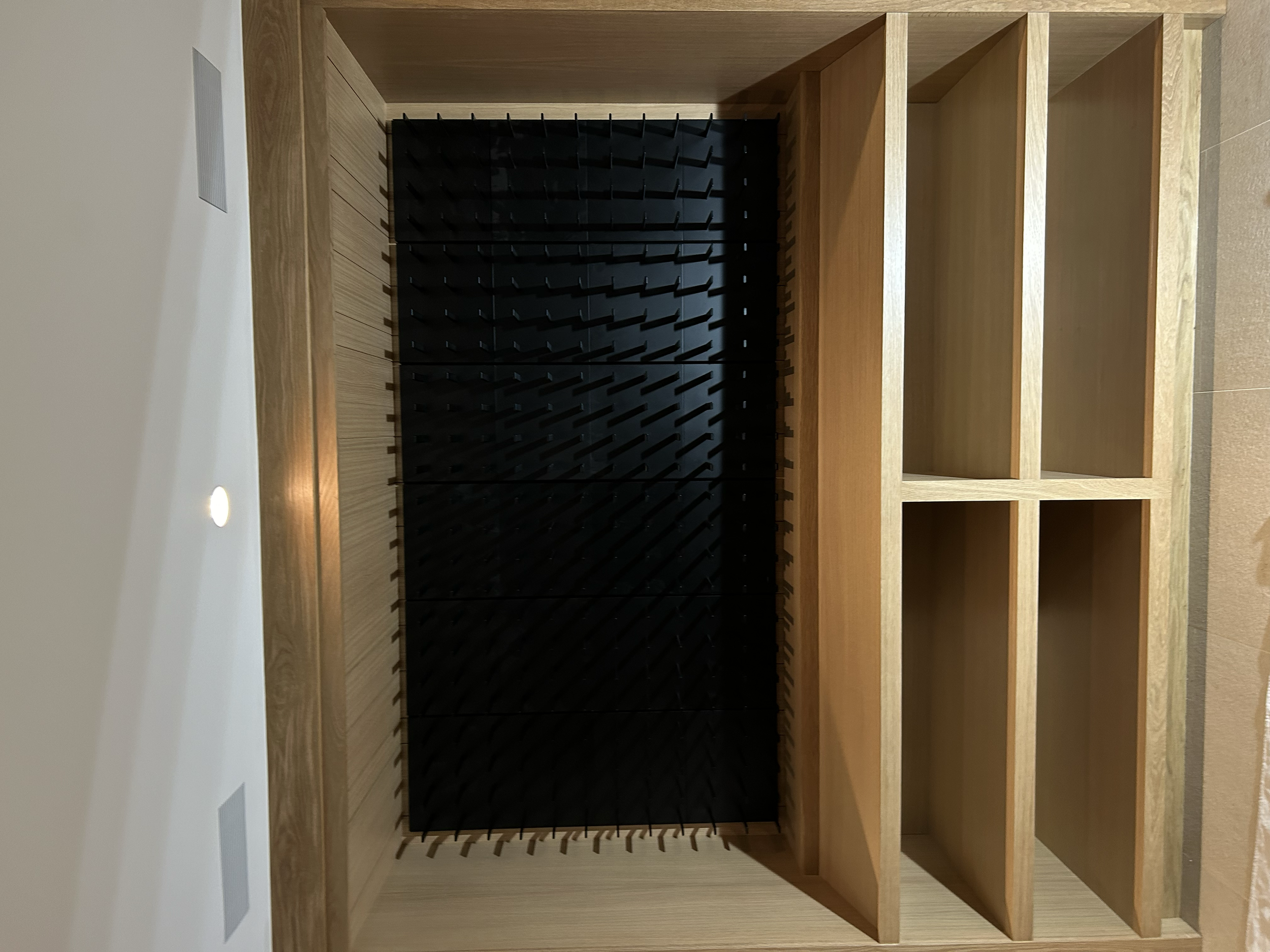 A wooden wine rack with a black wine bottle holder compartment on the left and empty shelves on the right.
