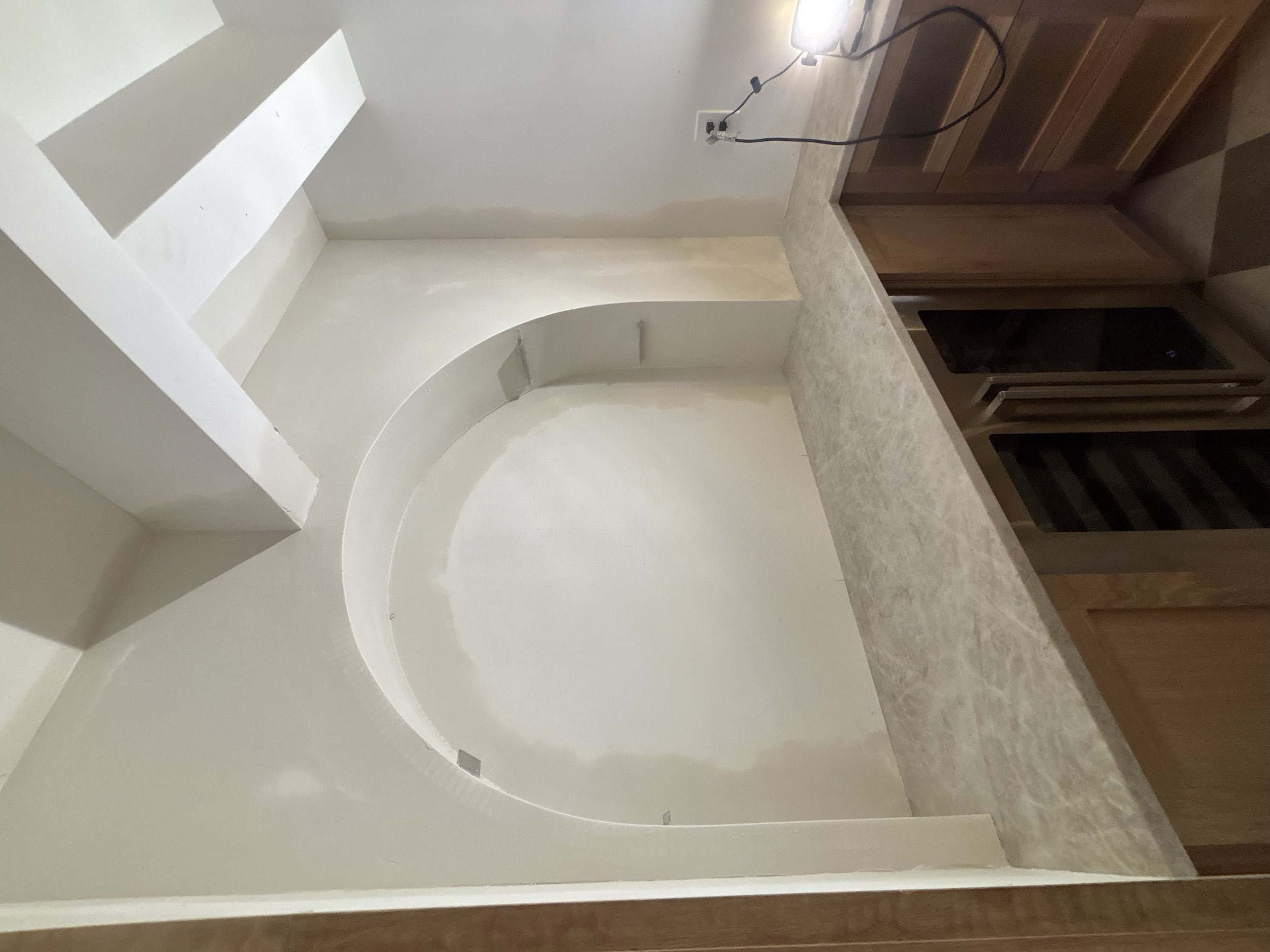 Empty kitchen with beige-colored countertop and wooden cabinets, electrical outlet with cord, and a small built-in wine rack.Walk in pantry. Custom Cabinetry.