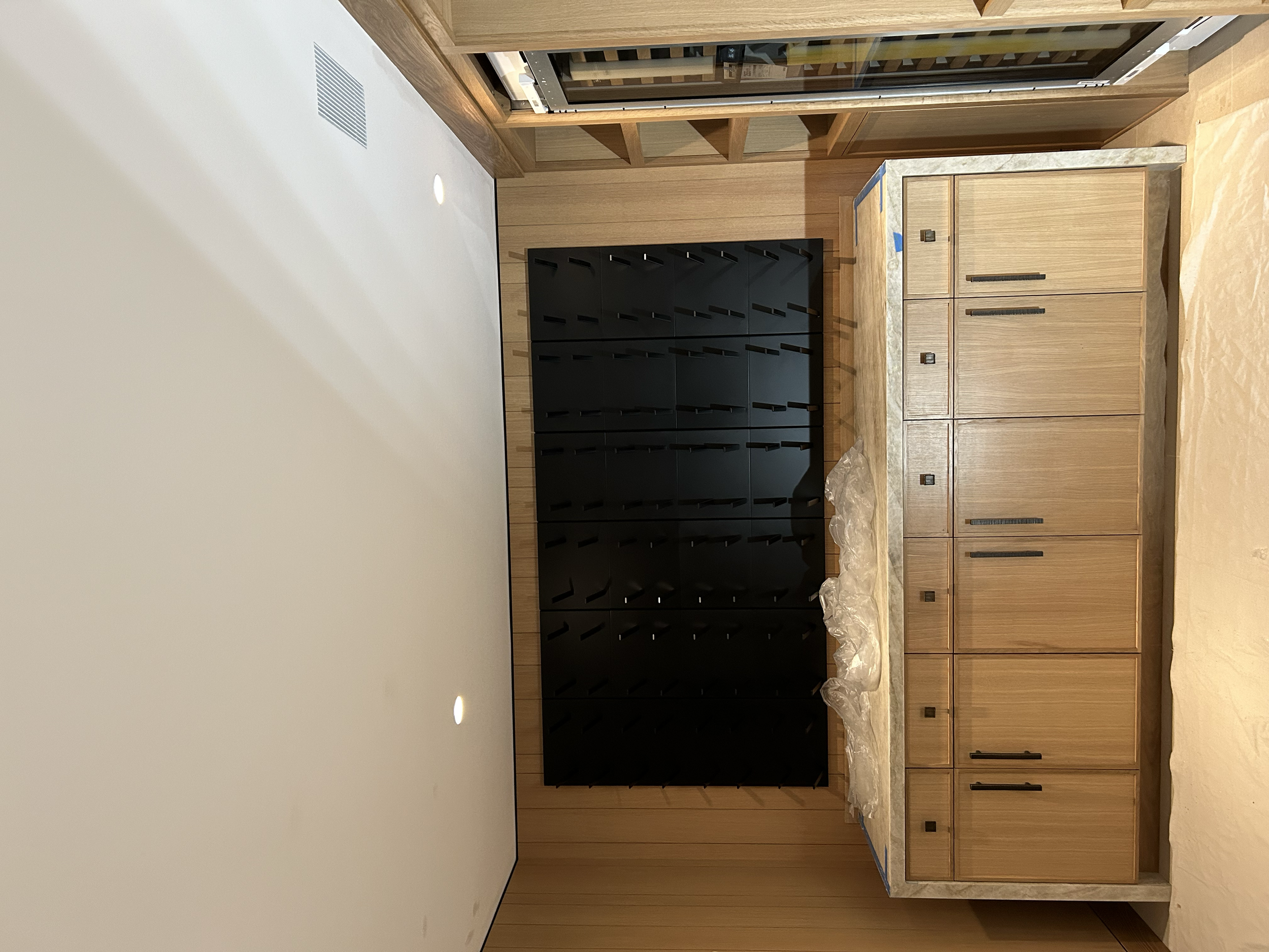 Interior of a room with wooden cabinetry, a marble countertop, and a black shelving unit, with a white ceiling and wooden wall paneling.