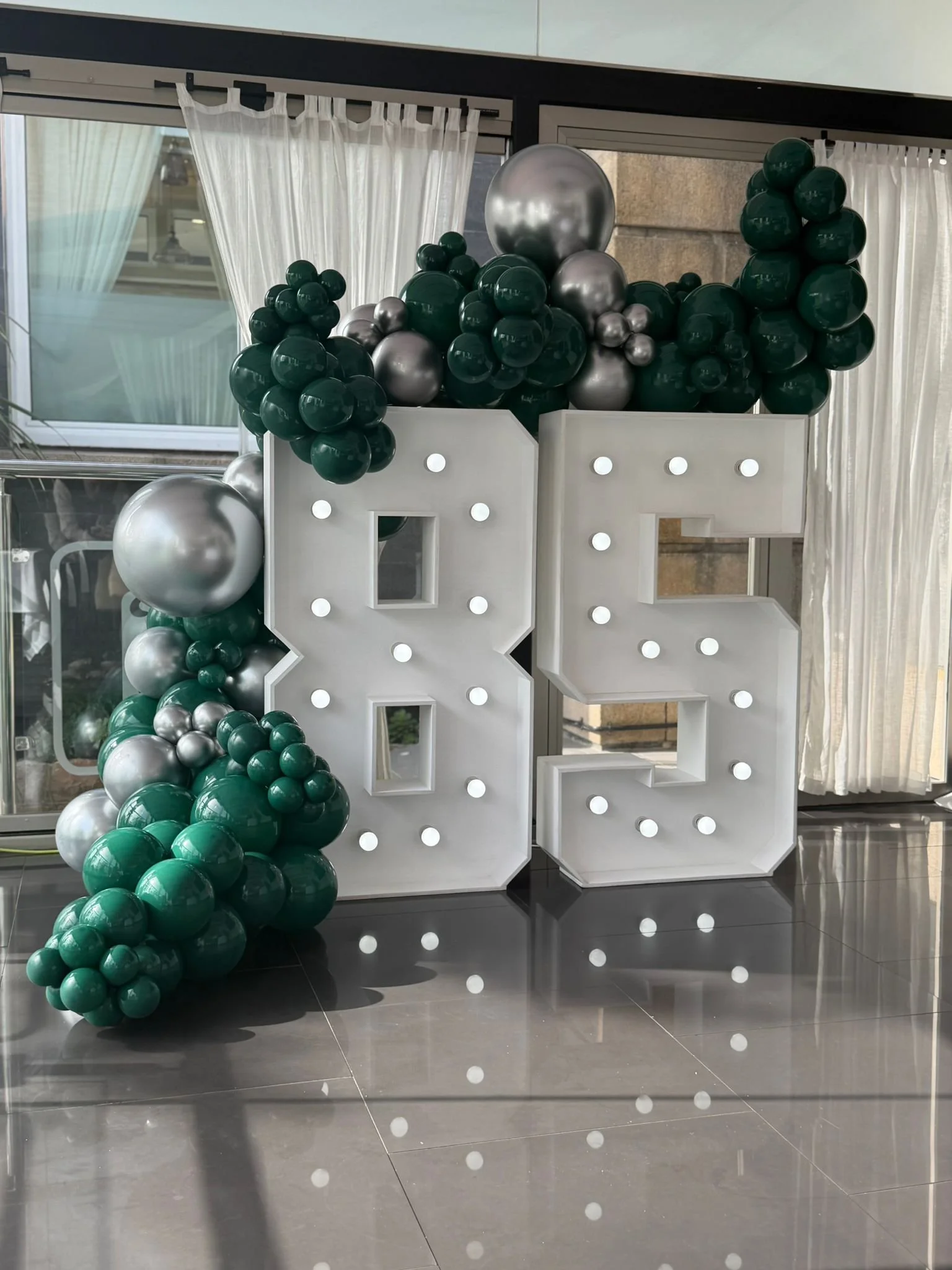 Decorative setup with large illuminated Z and O letters surrounded by gold, white, and cream balloons, with some small decorative wheat sheaves, likely for a celebration or milestone event.