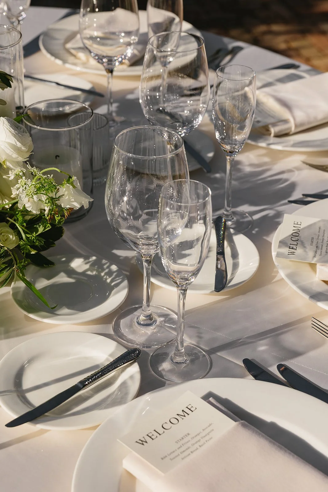Light blue wedding shoes with bows, a framed photo of a couple, wedding invitation, a small heart-shaped card that says 'Happy Tears', decorative lace and ribbon, a photo of the same couple, and a pearl hair accessory on a wooden surface.