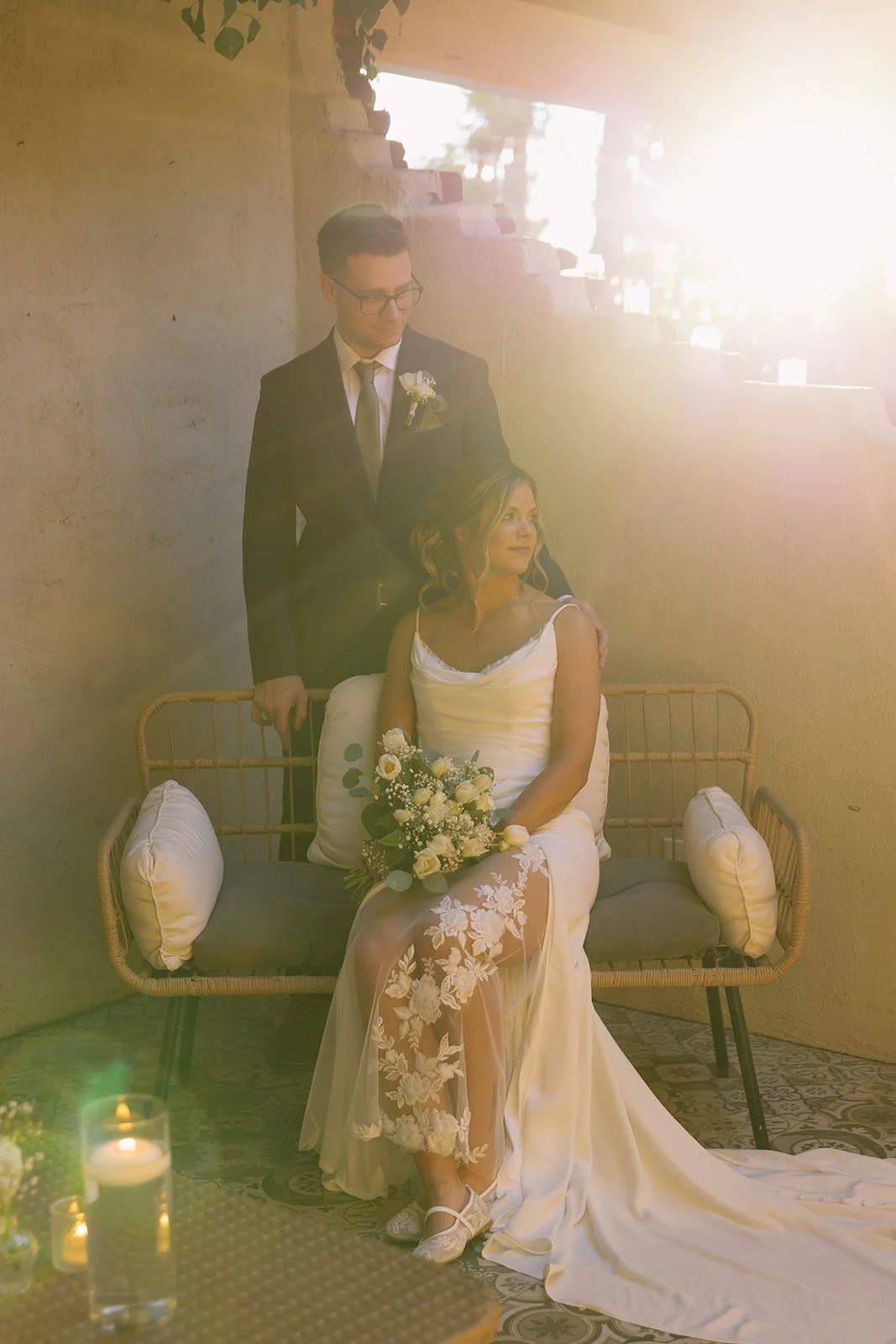 A black and white photo of a smiling bride and groom running on a rocky dirt road in a desert landscape, with mountains in the background.