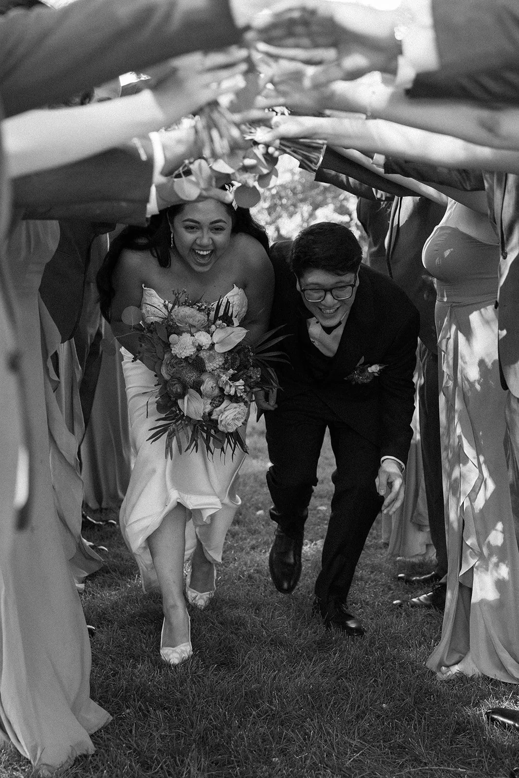 A bride and groom running through a decorated archway in their wedding celebration, surrounded by friends and family.