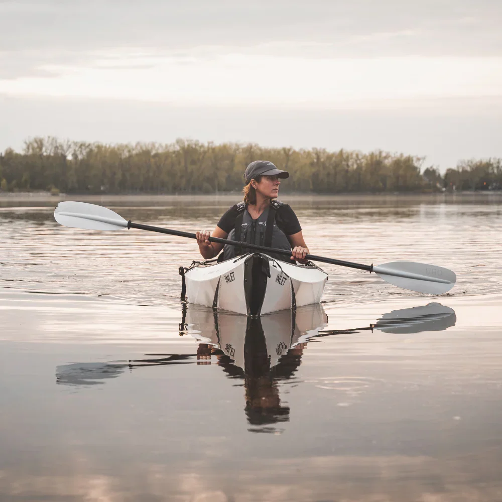 A person kayaking on calm water during sunrise or sunset with birds flying in the sky.