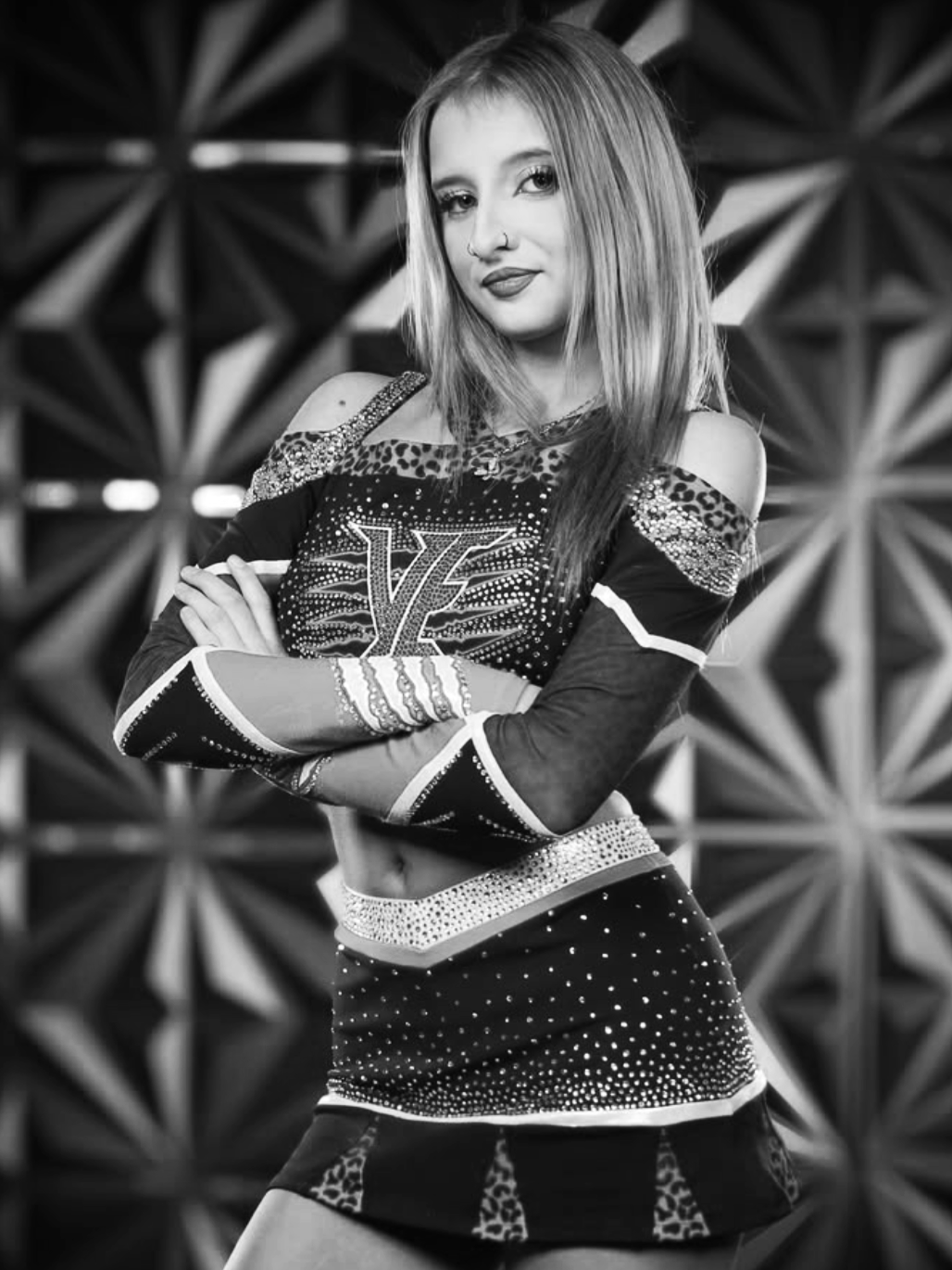 Black and white photo of a young woman with shoulder-length hair, crossed arms, and a confident expression, standing in front of a geometric patterned background.