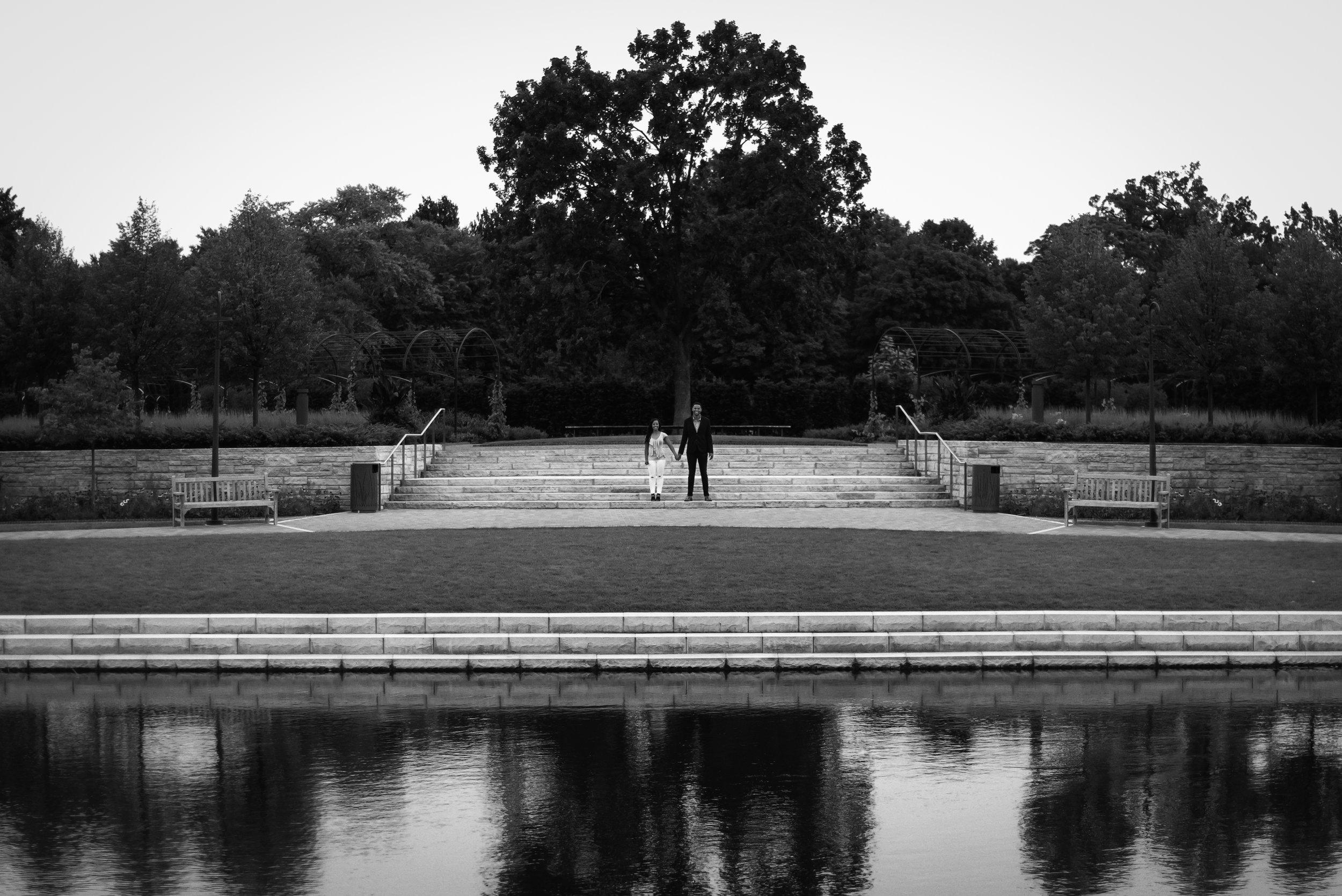 Black and white engagement portrait of couple framed by modern architecture and water reflection