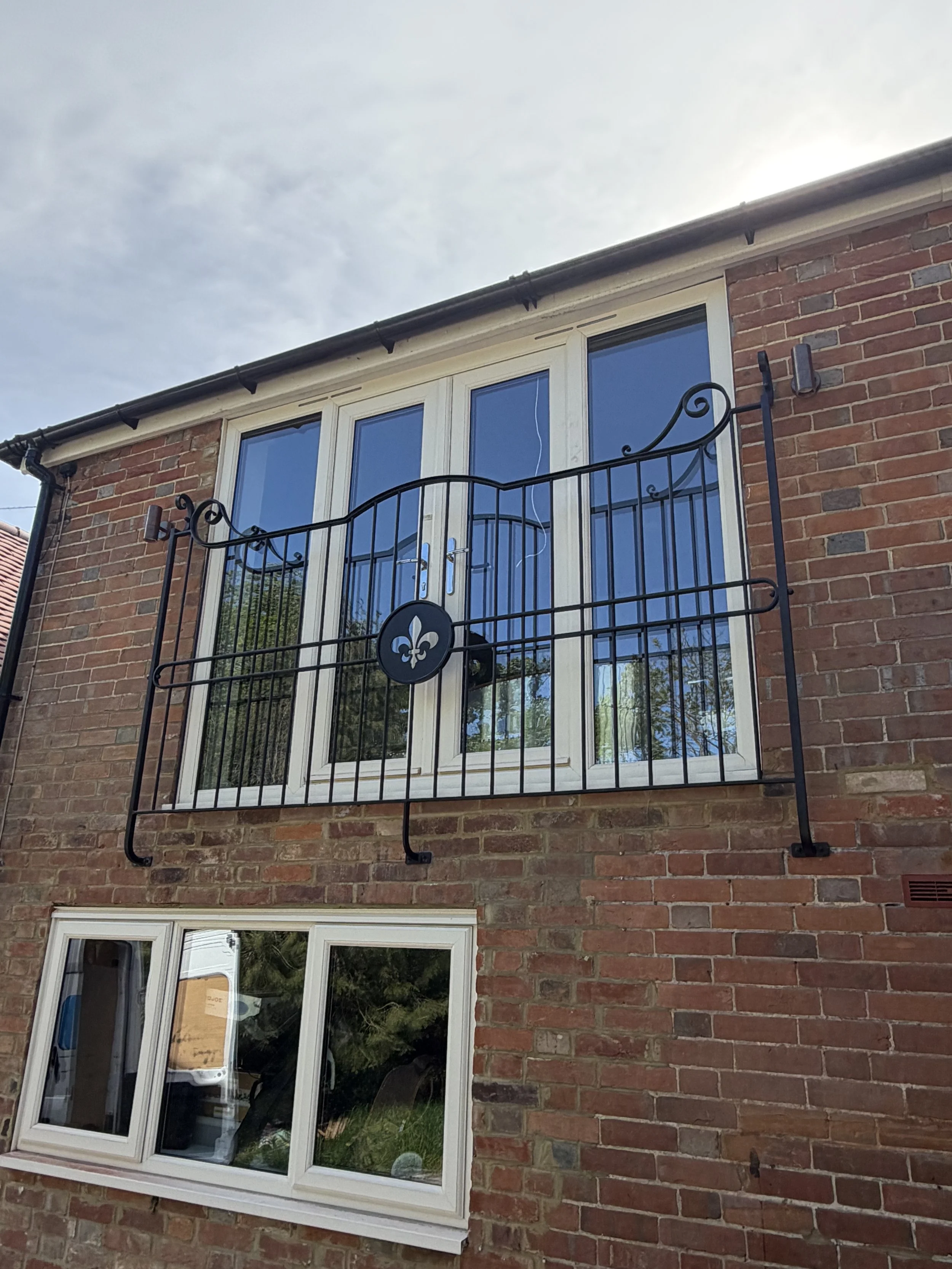 Bespoke steel Juliet balcony in Tenterden, Kent, featuring traditional forged scrollwork and a central fleur-de-lis detail.