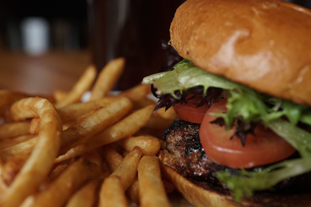 Close-up of a burger with lettuce, tomato, and a beef patty, served with French fries.
