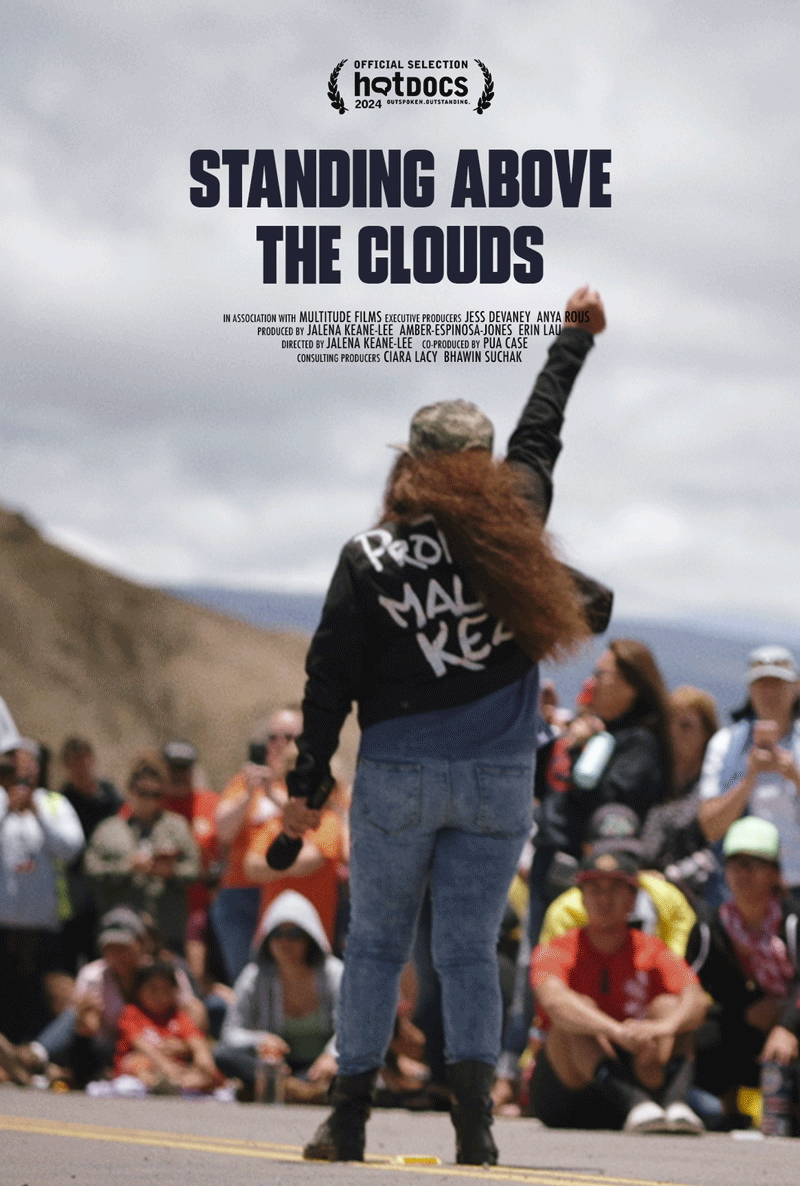 A person raising a fist with her back turned to the camera and facing a crowd of onlookers