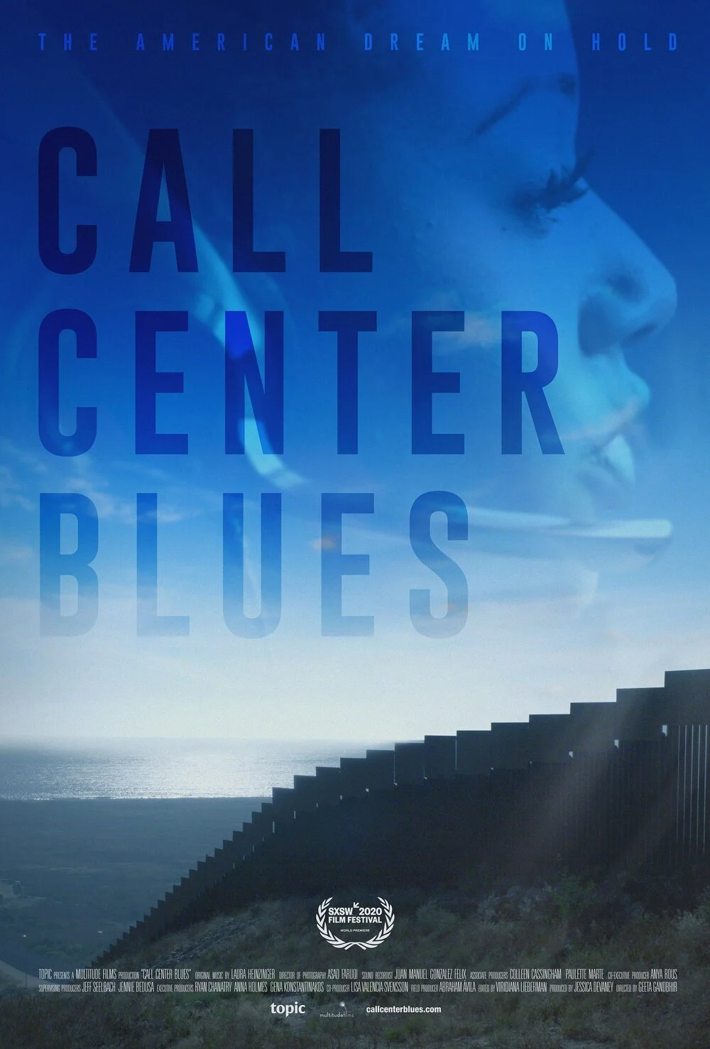 Call Center Blues film poster shows a border wall stretching into the distance, with white clouds and blue sky above it. A close-up profile of a person with long eye lashes and a headset on is imposed on the negative space of the sky above the wall.