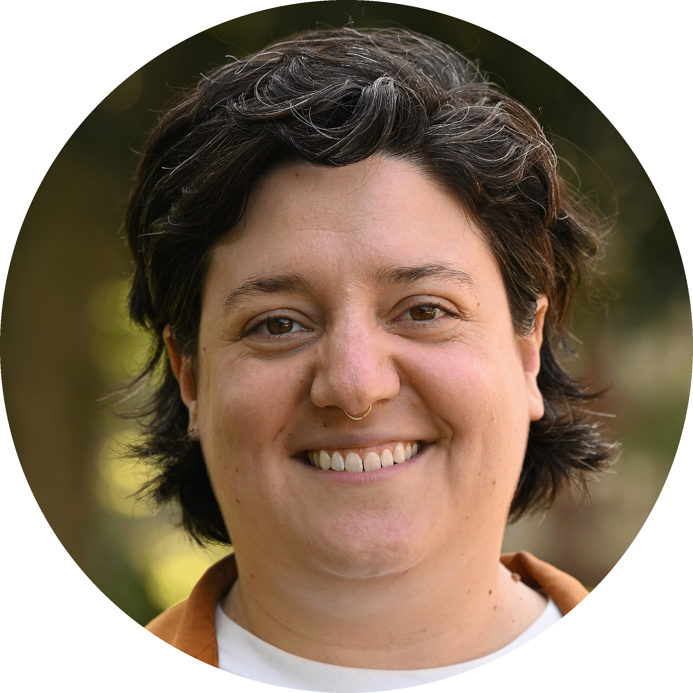 Noah is a fair-skinned person with short, dark hair. They are wearing a dotted navy shirt against a grey backdrop.