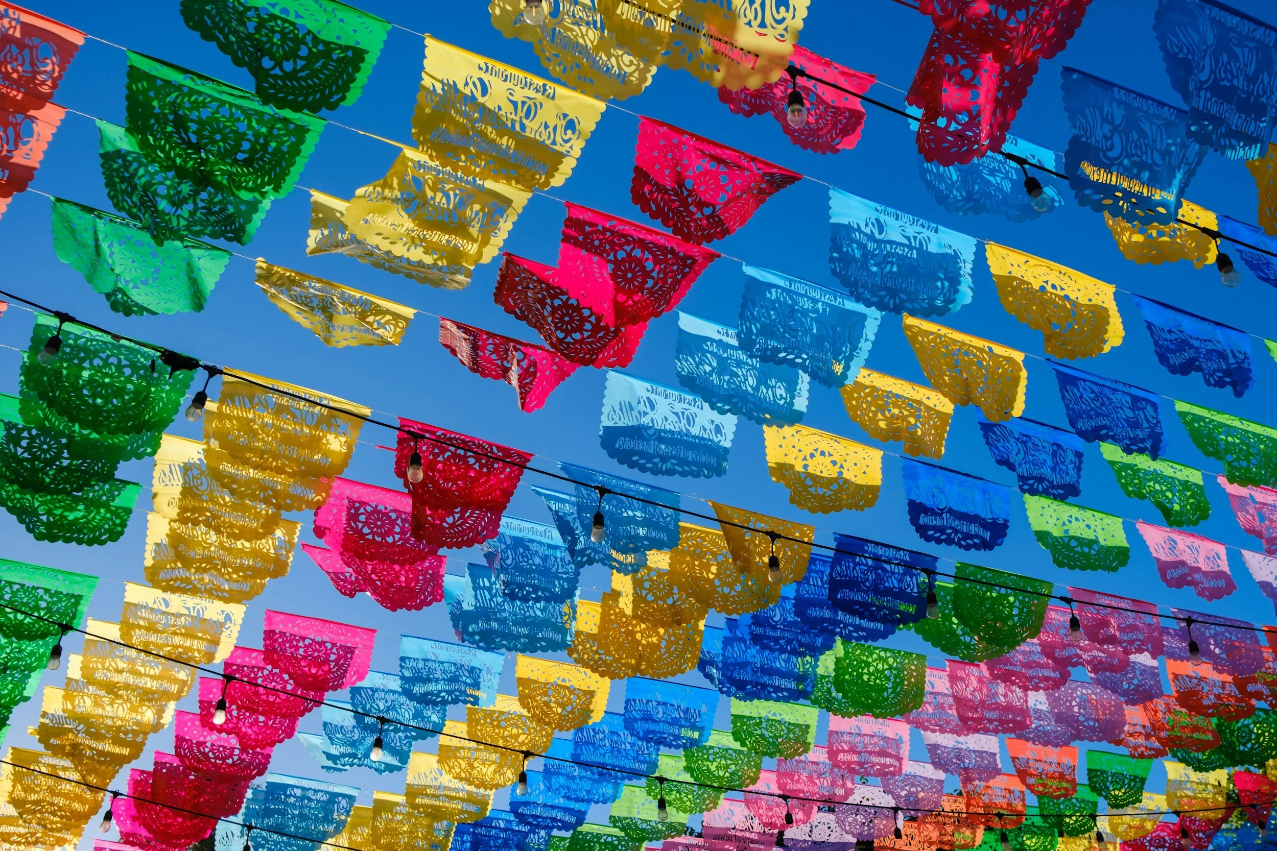 Colorful papel picado banners hanging against a clear blue sky.