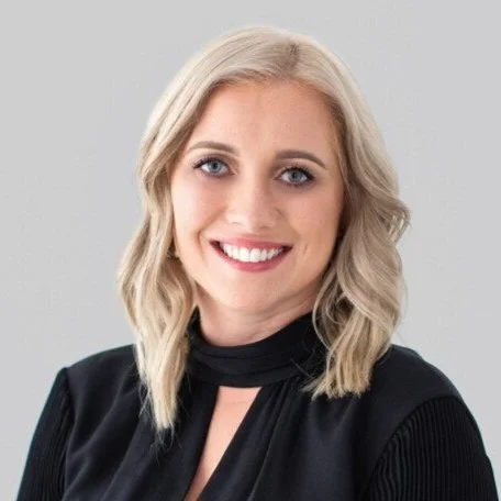 Smiling woman with blonde hair wearing a black top against a neutral background.