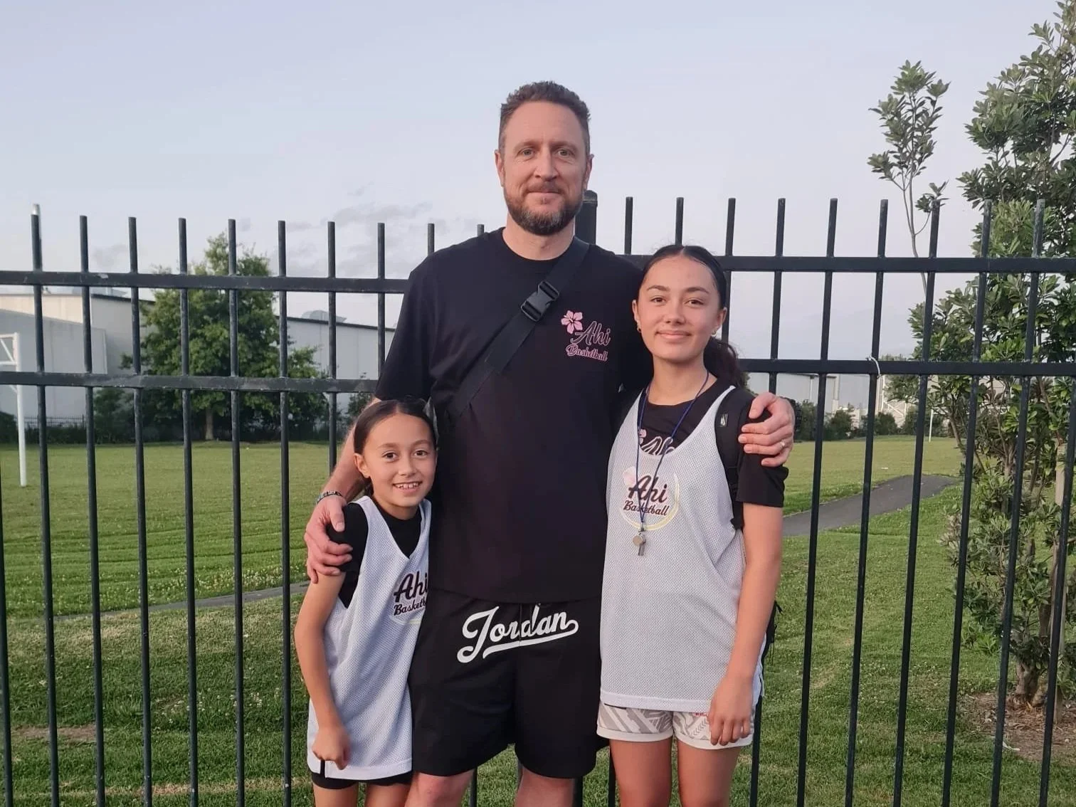 Dad and his two daughters in Ahi Basketball uniforms, showcasing family support, youth basketball development, girls basketball, and community sport at Auckland's Ahi Basketball Club.