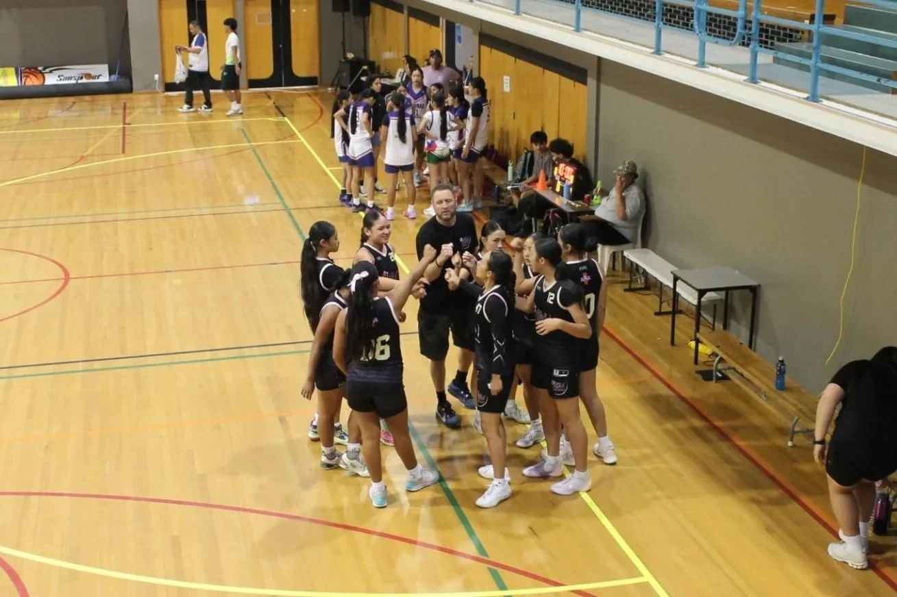 Girls volleyball team huddled with coach during game break in gymnasium.