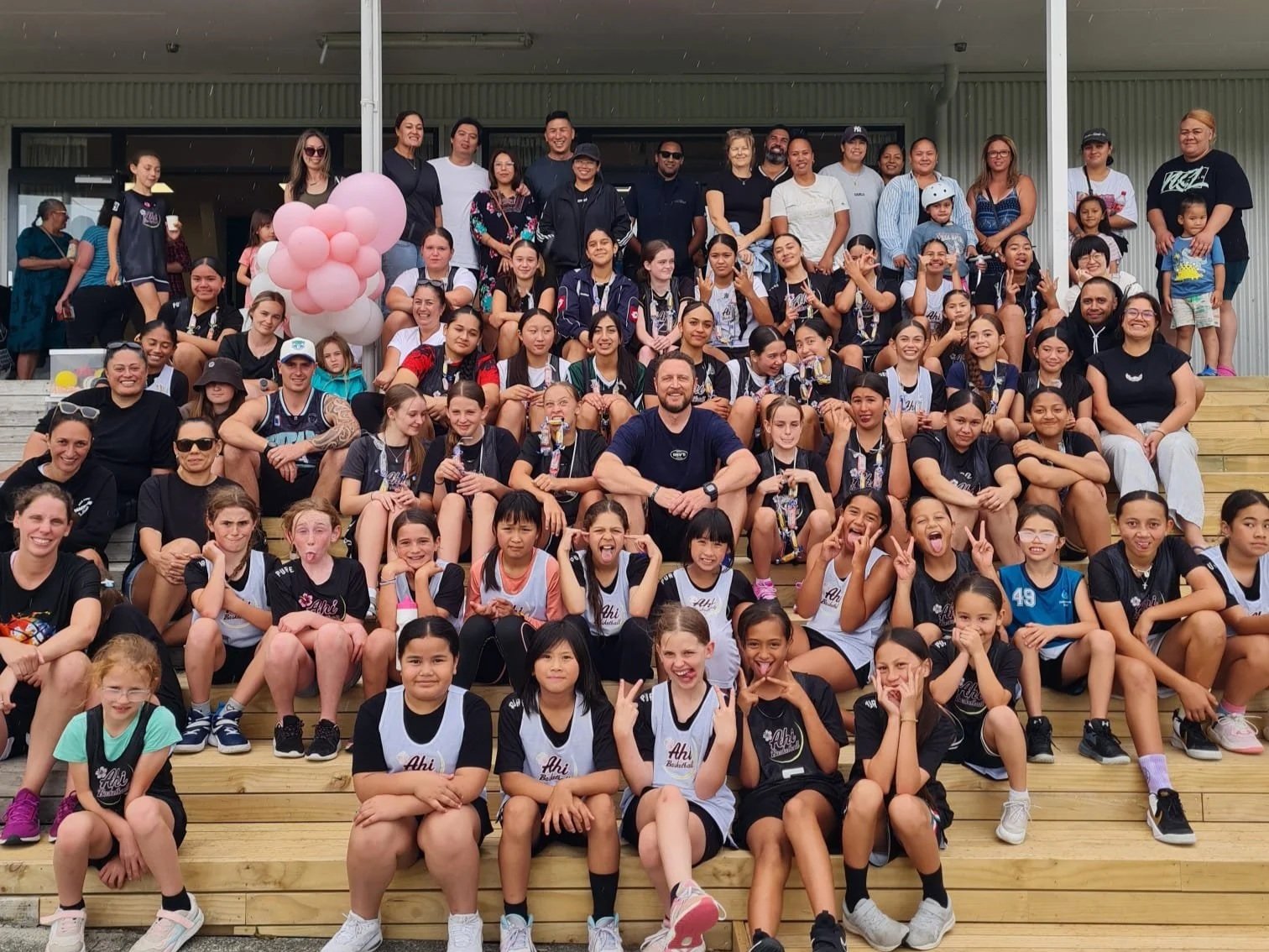 Ahi Basketball club players, coaches, and families gathered on steps for a team photo, showcasing Auckland girls basketball, youth athlete development, community spirit, and the Ahi Basketball whānau.
