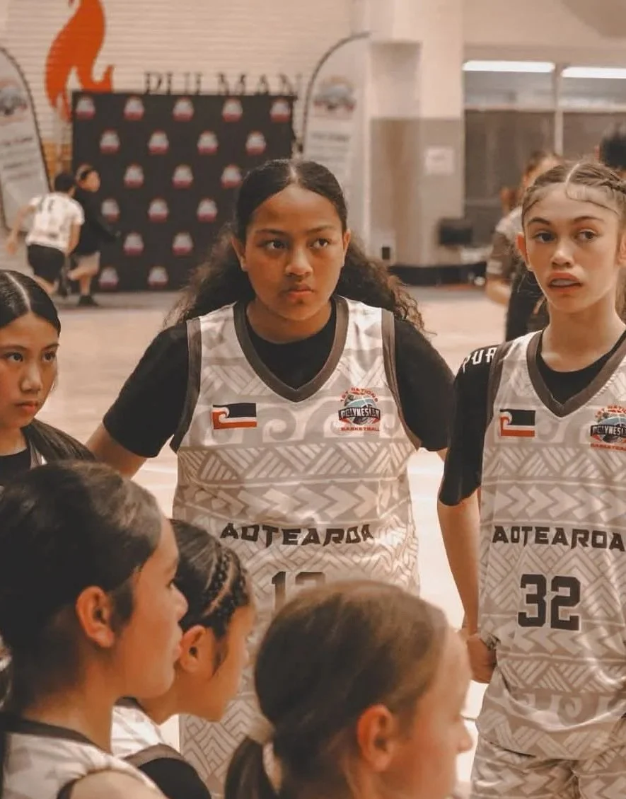 Young female basketball players listening to coach during a team huddle in a gymnasium.