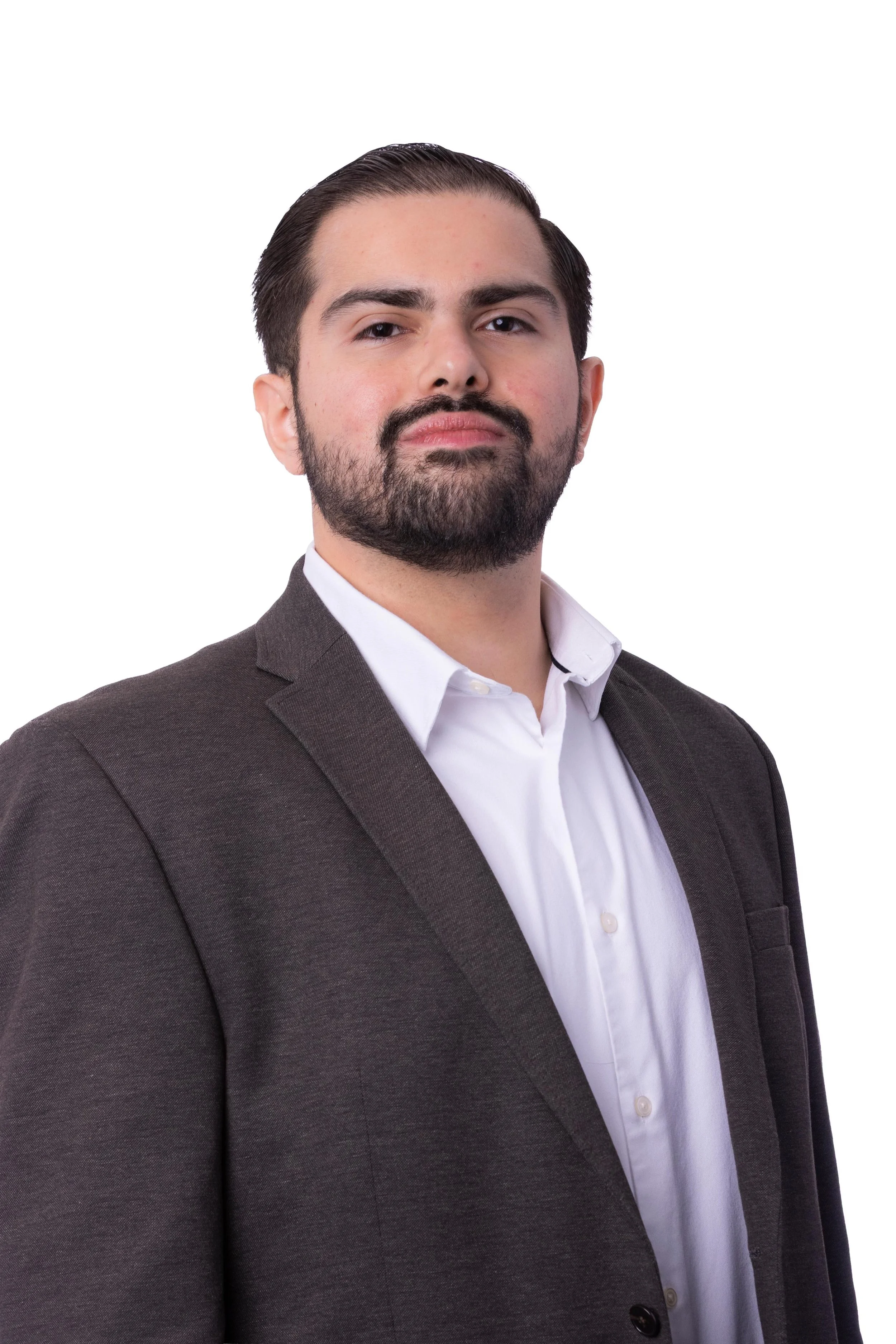 Retrato de un hombre con barba y cabello oscuro peinado hacia atrás, vestido con saco gris y camisa blanca, contra fondo blanco.
