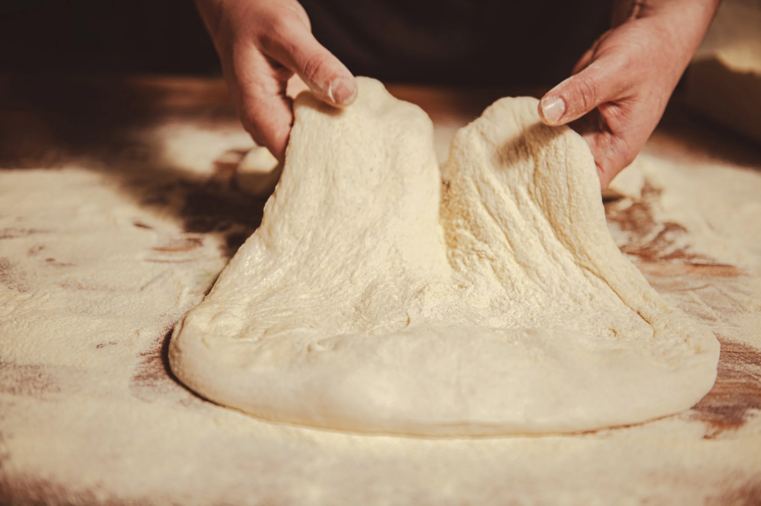 Close-up of hands kneading dough on a wooden surface.