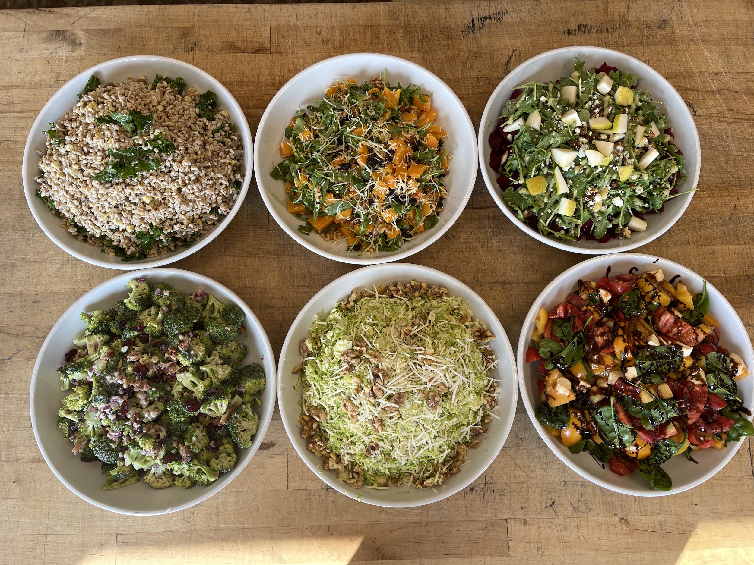 Various bowls of colorful salads on a wooden table.
