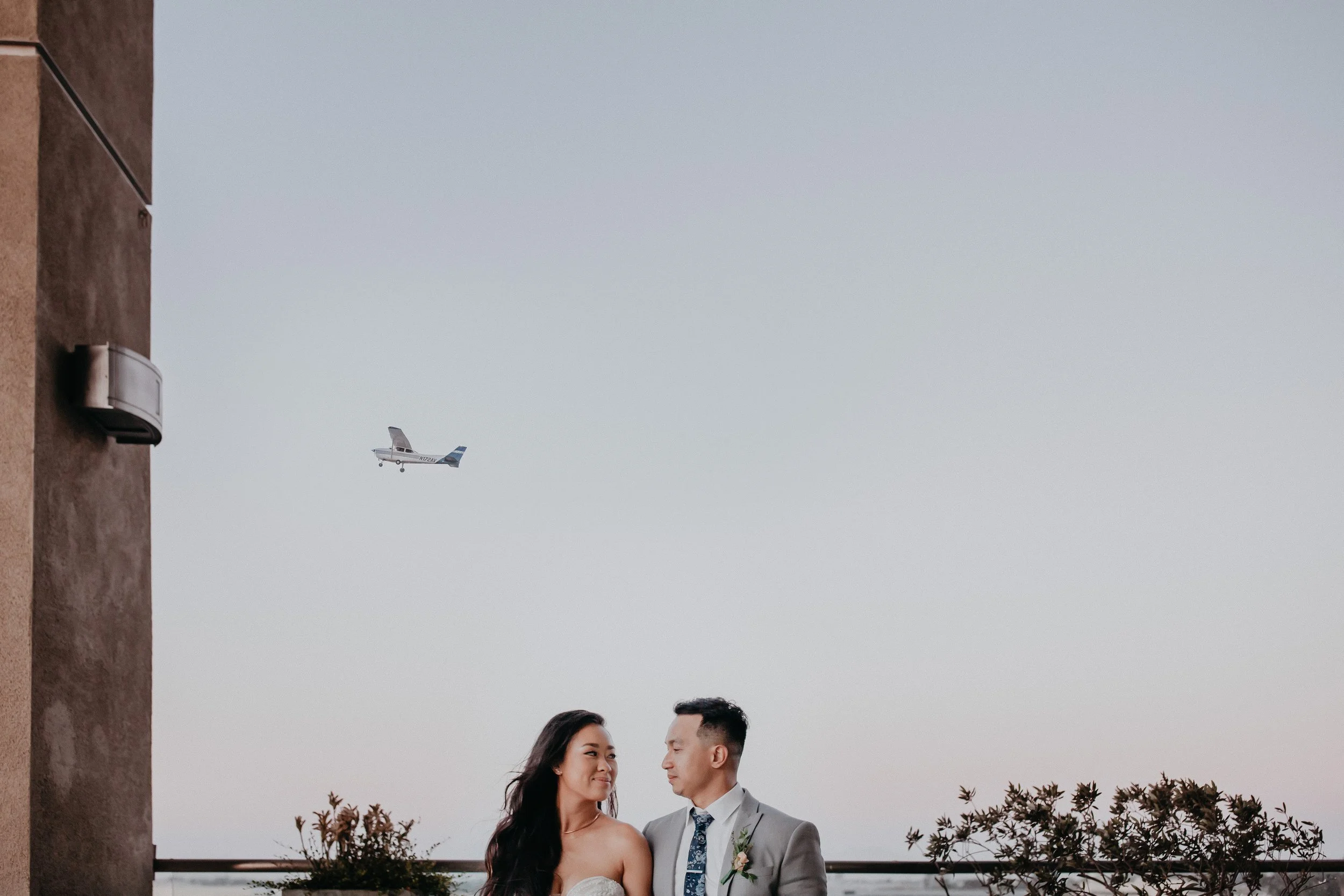 Couple in wedding attire on rooftop with plane overhead