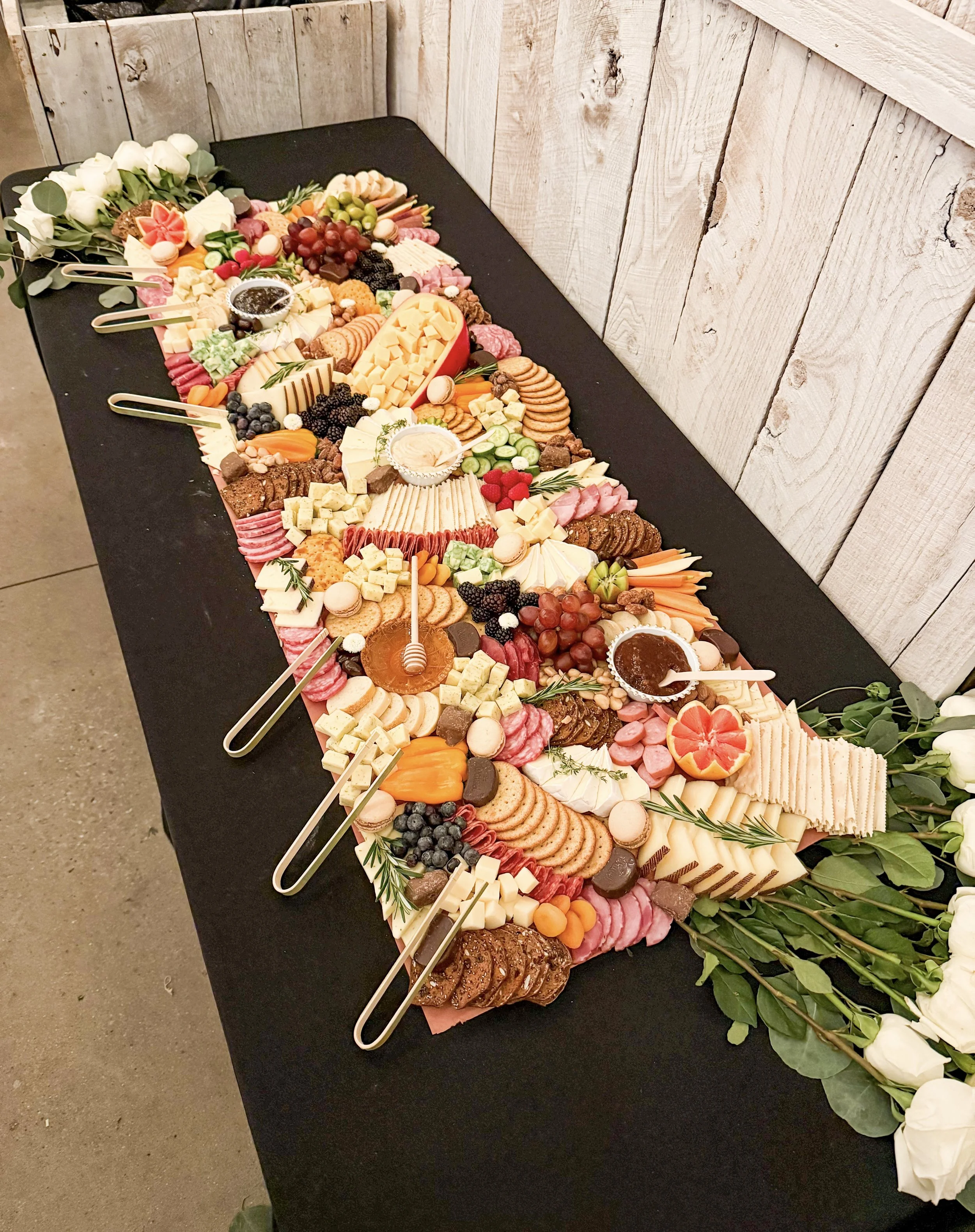 Four foot wedding grazing table with meats, cheeses, crackers, fresh fruit, vegetables, hummus, honey and jam with white roses accenting it.