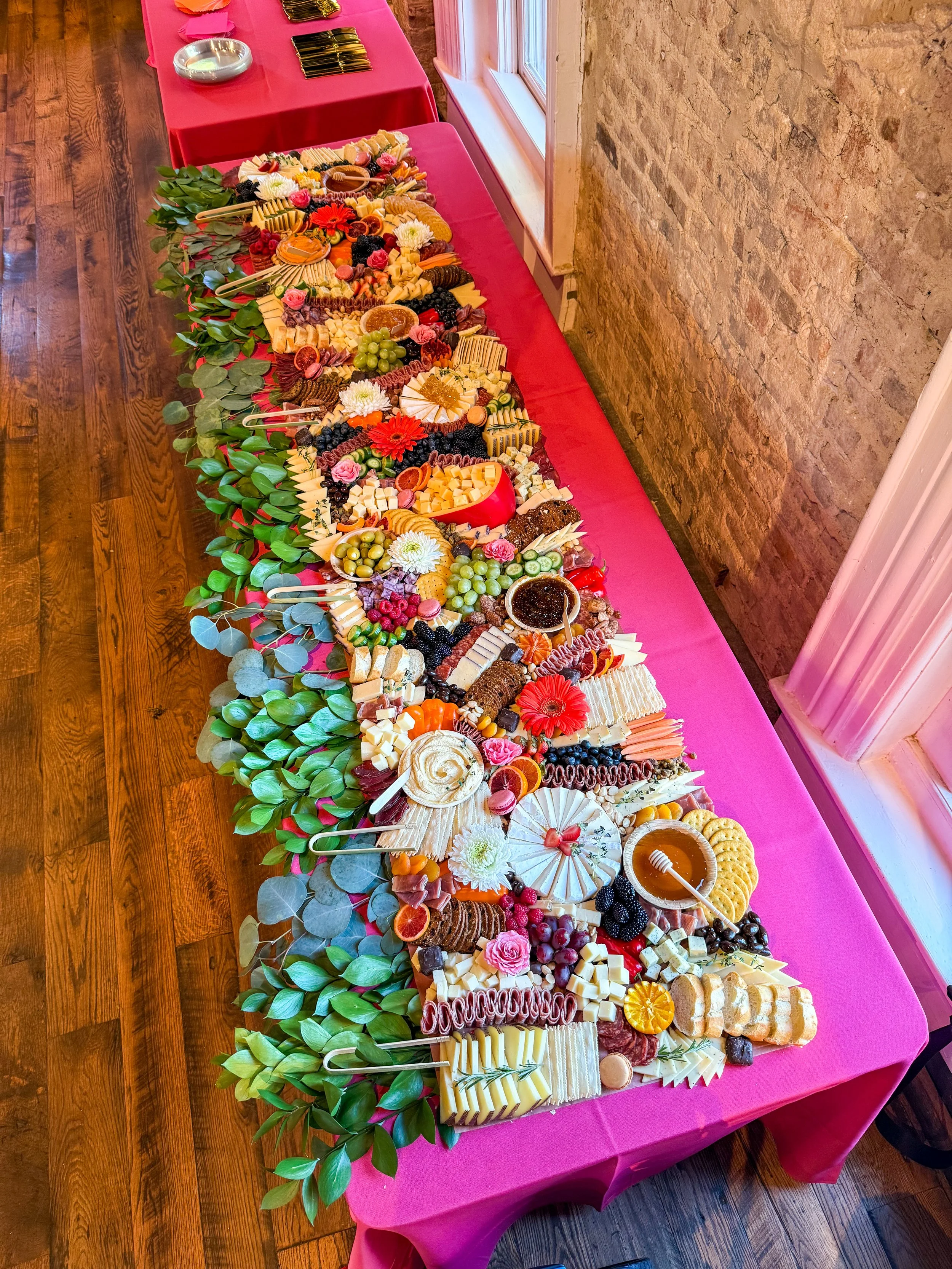 Eight foot grazing table with meats, cheeses, crackers, fresh fruit, honey and jam with greenery outlining it. 