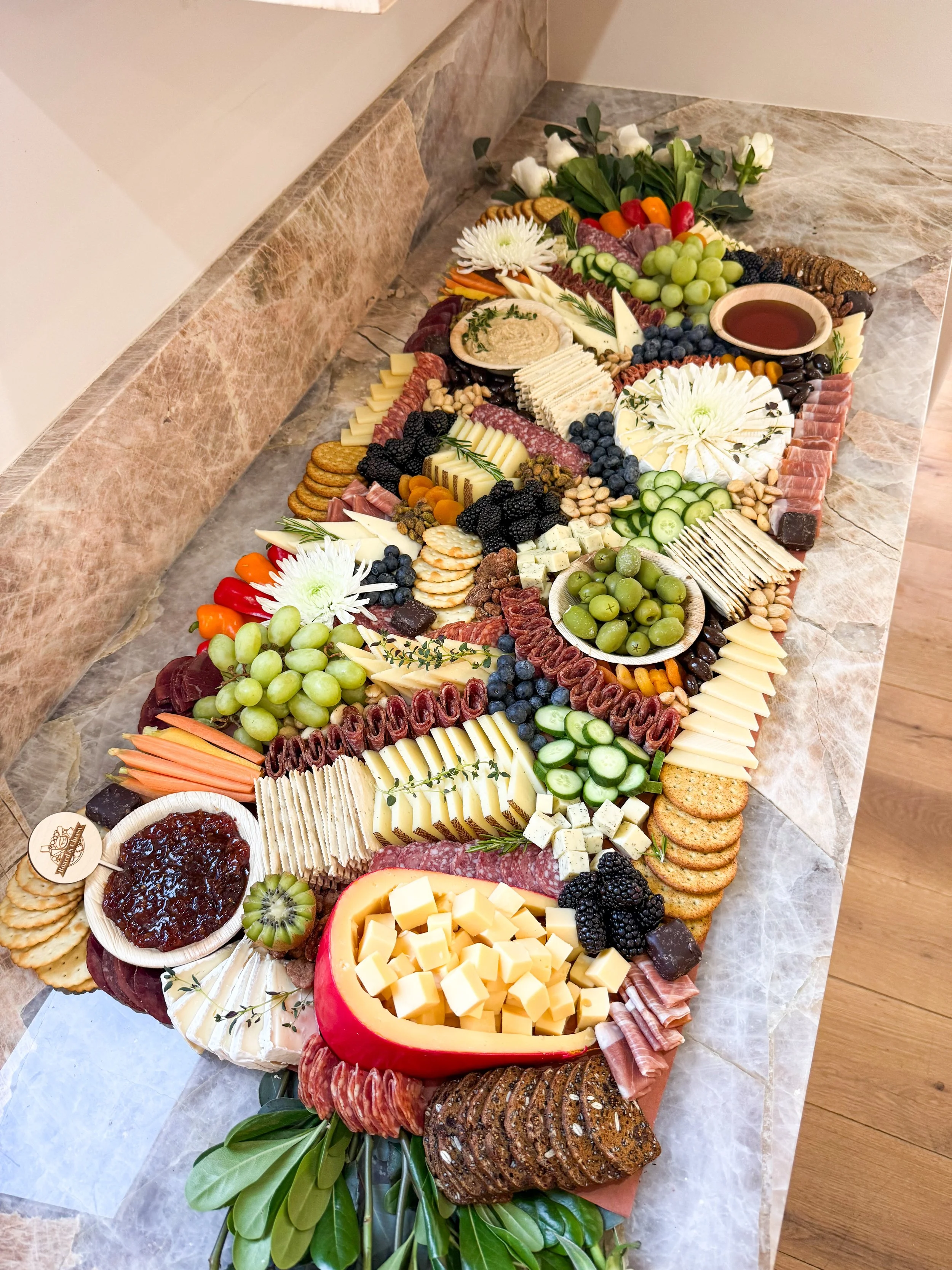 Three foot grazing table with meats, cheeses, crackers, fresh fruit, honey and jam with greenery and white roses outlining it.